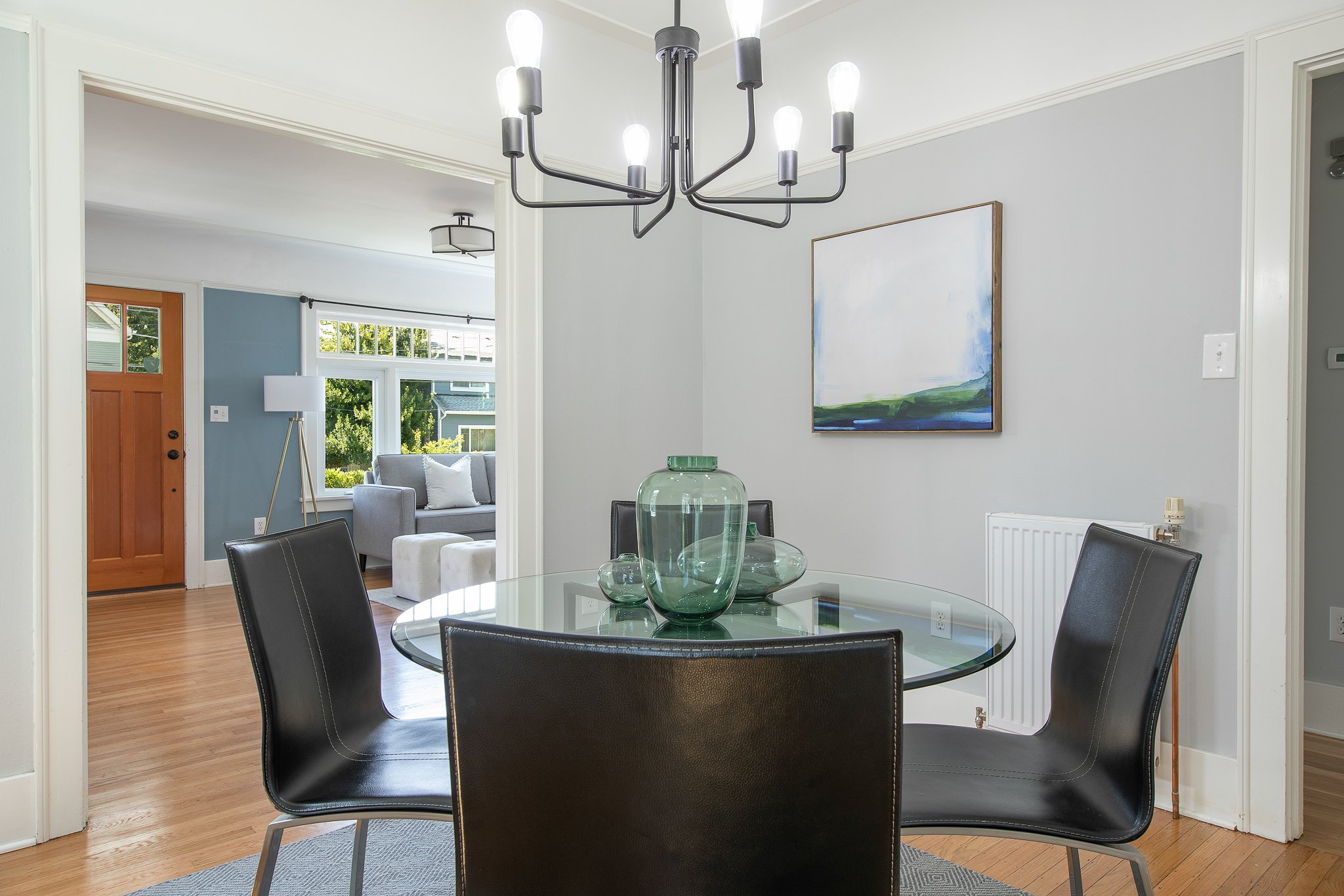 View of dining area with a black glass table, black chairs, green glass vases, and a chandelier in a modern home interior.