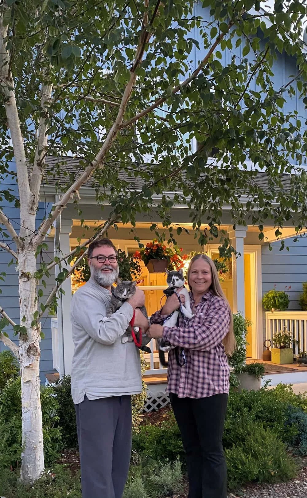 First-time homebuyers standing outside their new home with their cats. 
