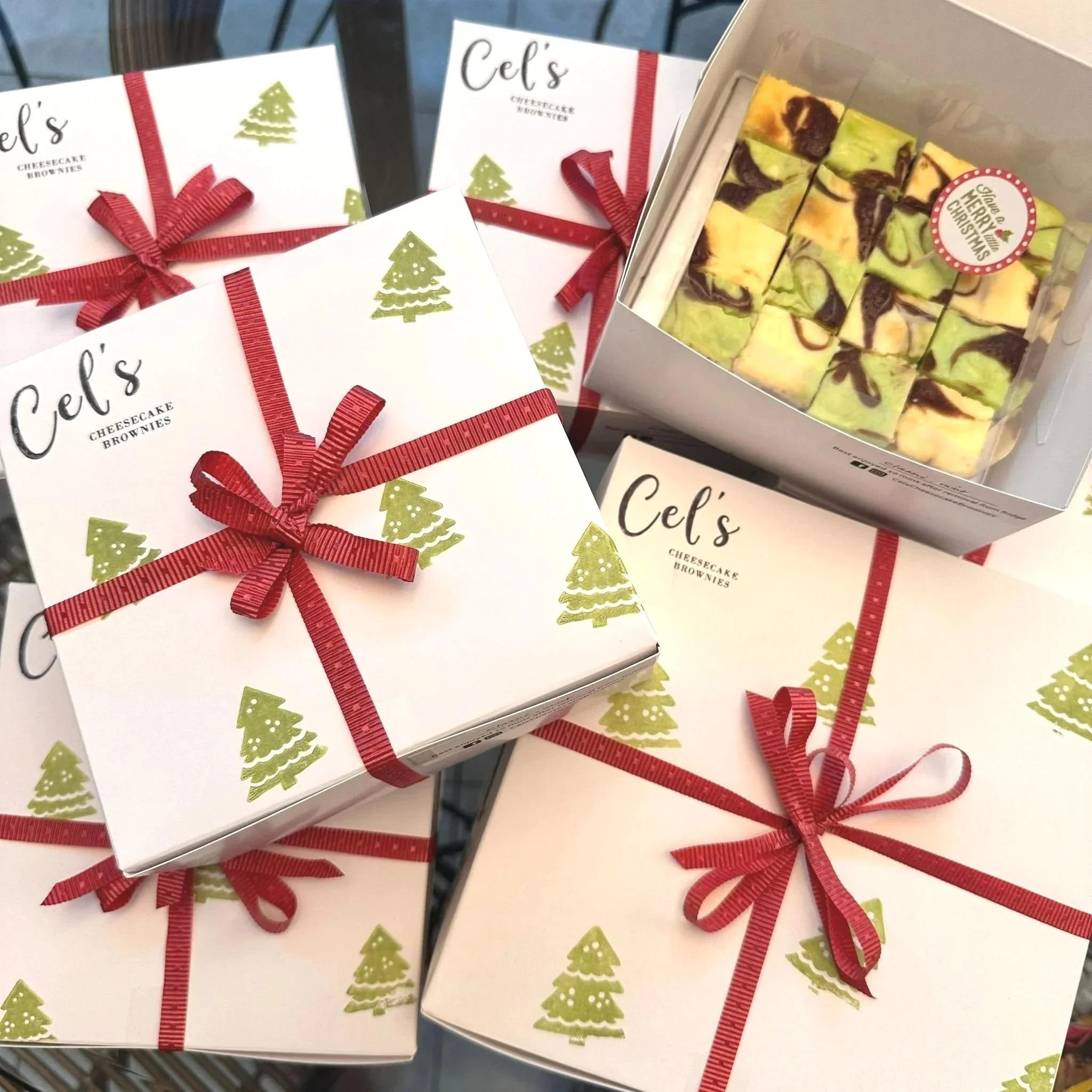 Boxes of cheesecake brownies wrapped with red ribbons, decorated with Christmas-themed prints and a box of marble-finished cheesecake brownies with a "Merry Christmas" sticker.