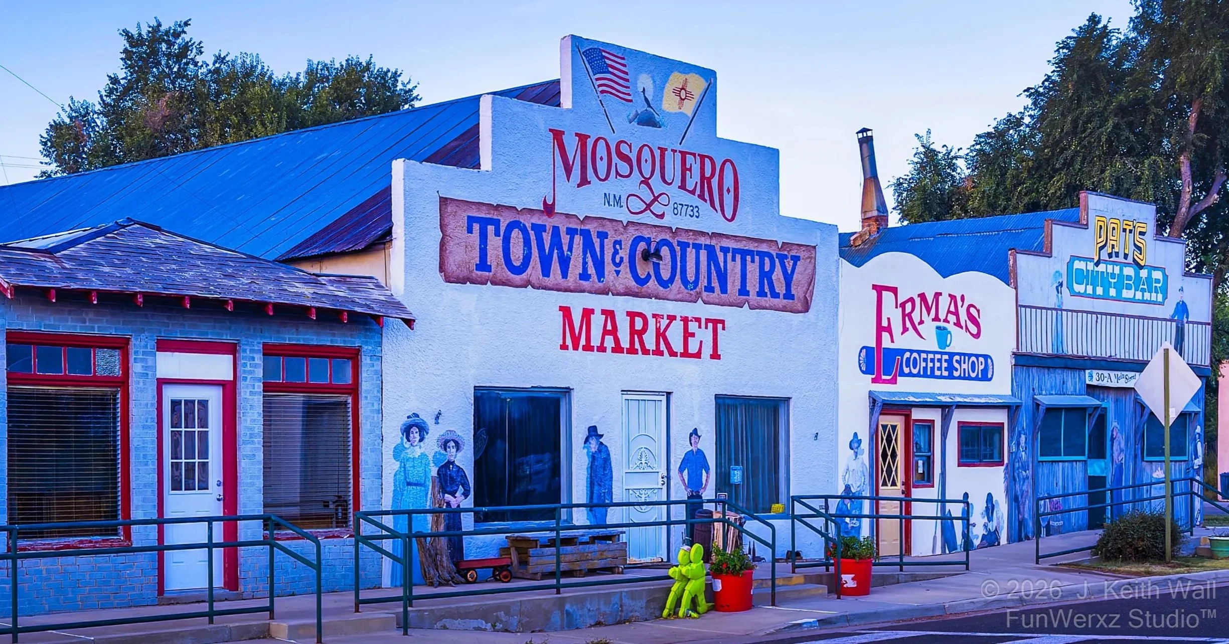 Painted building facades in a small town, featuring signs for Mosquero Town & Country Market, Erma's Coffee Shop, and Pats City Bar. The buildings are decorated with cowboy and Western-themed murals, and there are painted figures of cowboys, cowgirls, and other Western motifs.