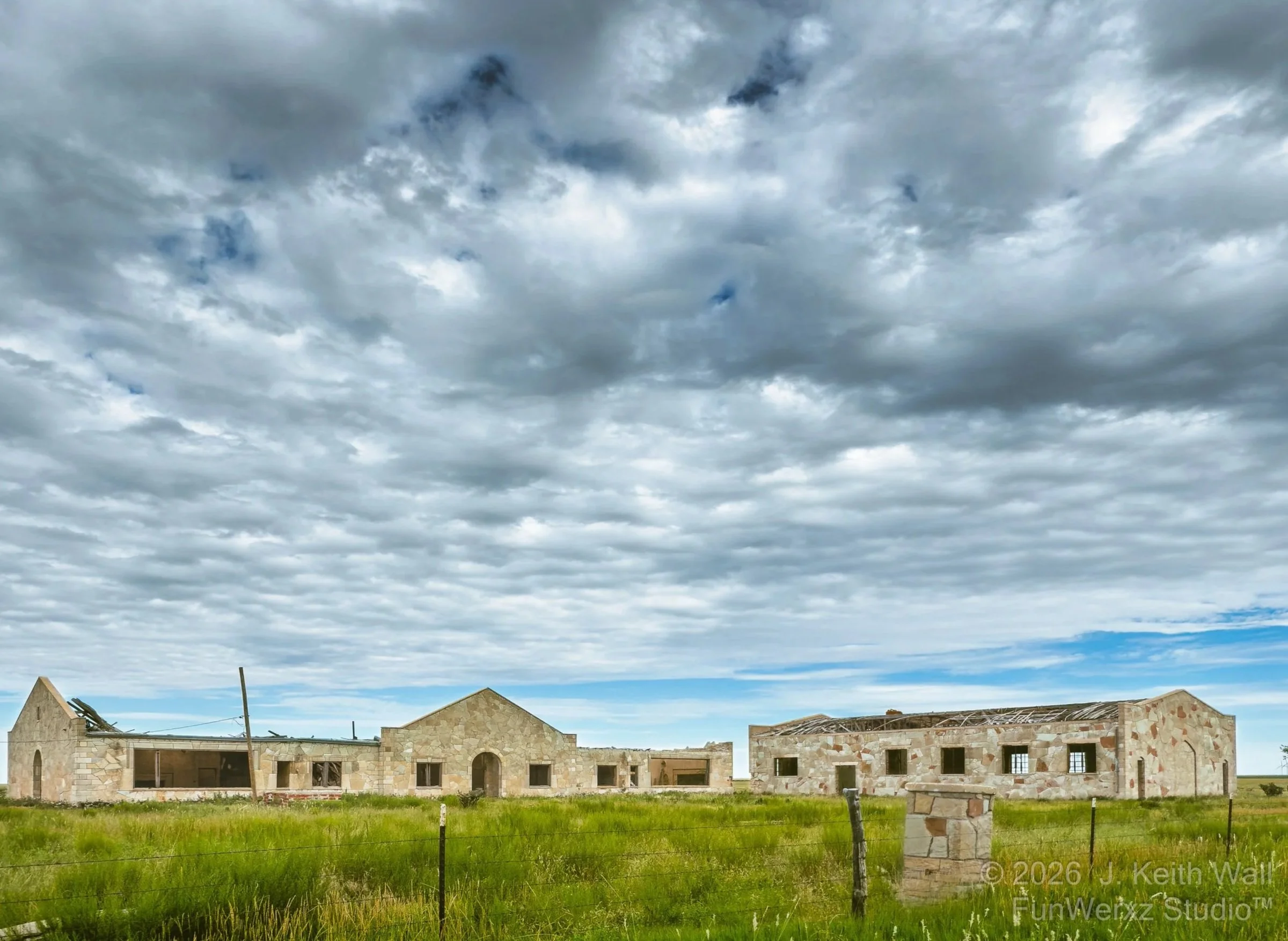 A cloudy sky over a partially constructed stone building with a green grassy field in the foreground.
