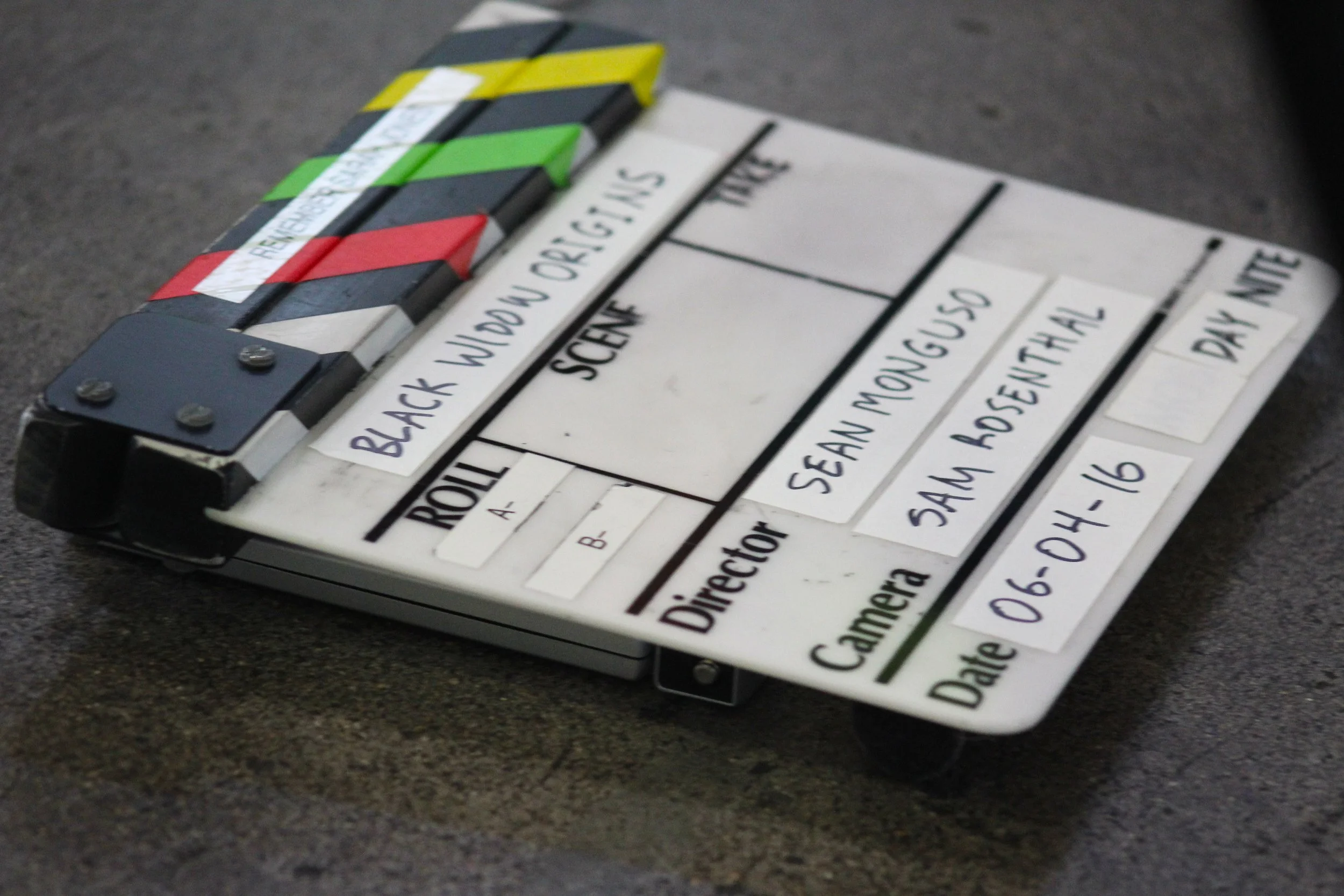 Clapperboard used in film production with handwritten labels and color tabs, resting on a dark surface.