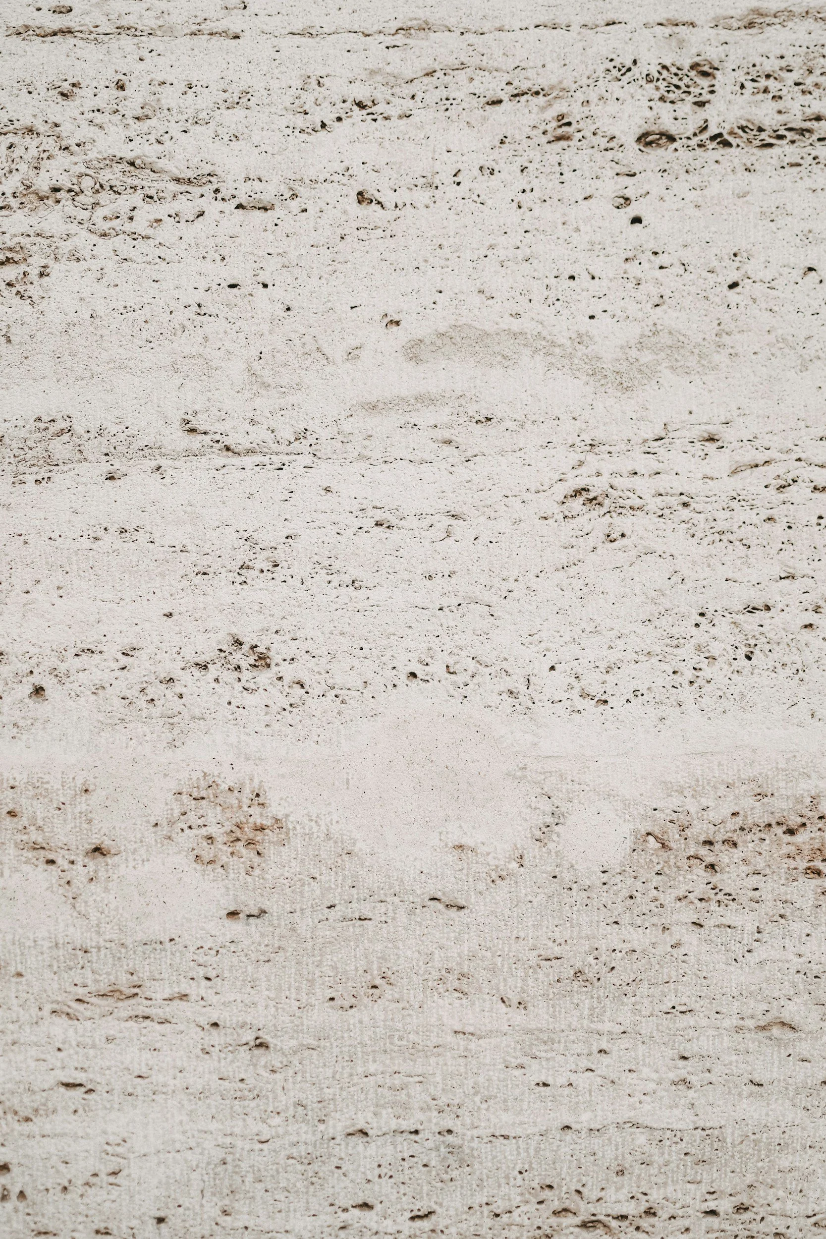 Close-up of beige textured brick wall with small imperfections and variations in color.