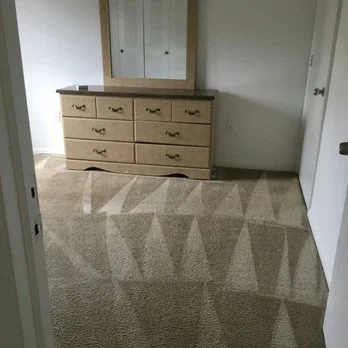 Empty bedroom with a wooden dresser, mirror, and carpeted floor.