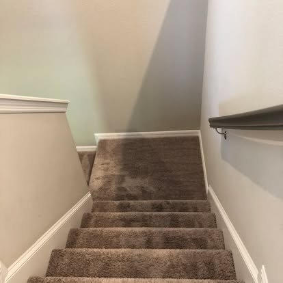 Staircase with brown carpet, white walls, white baseboard, and a black handrail on the right side.