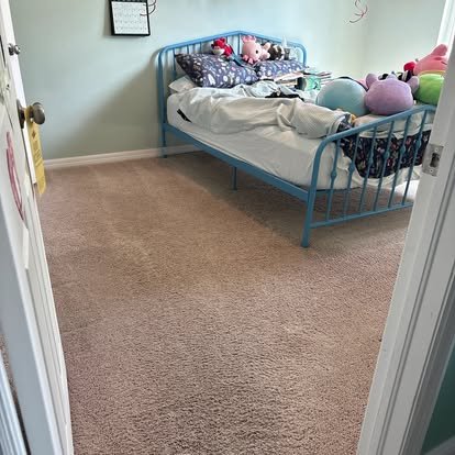 A bedroom with a light blue metal bed frame, stuffed animals on the bed, and a beige carpeted floor.