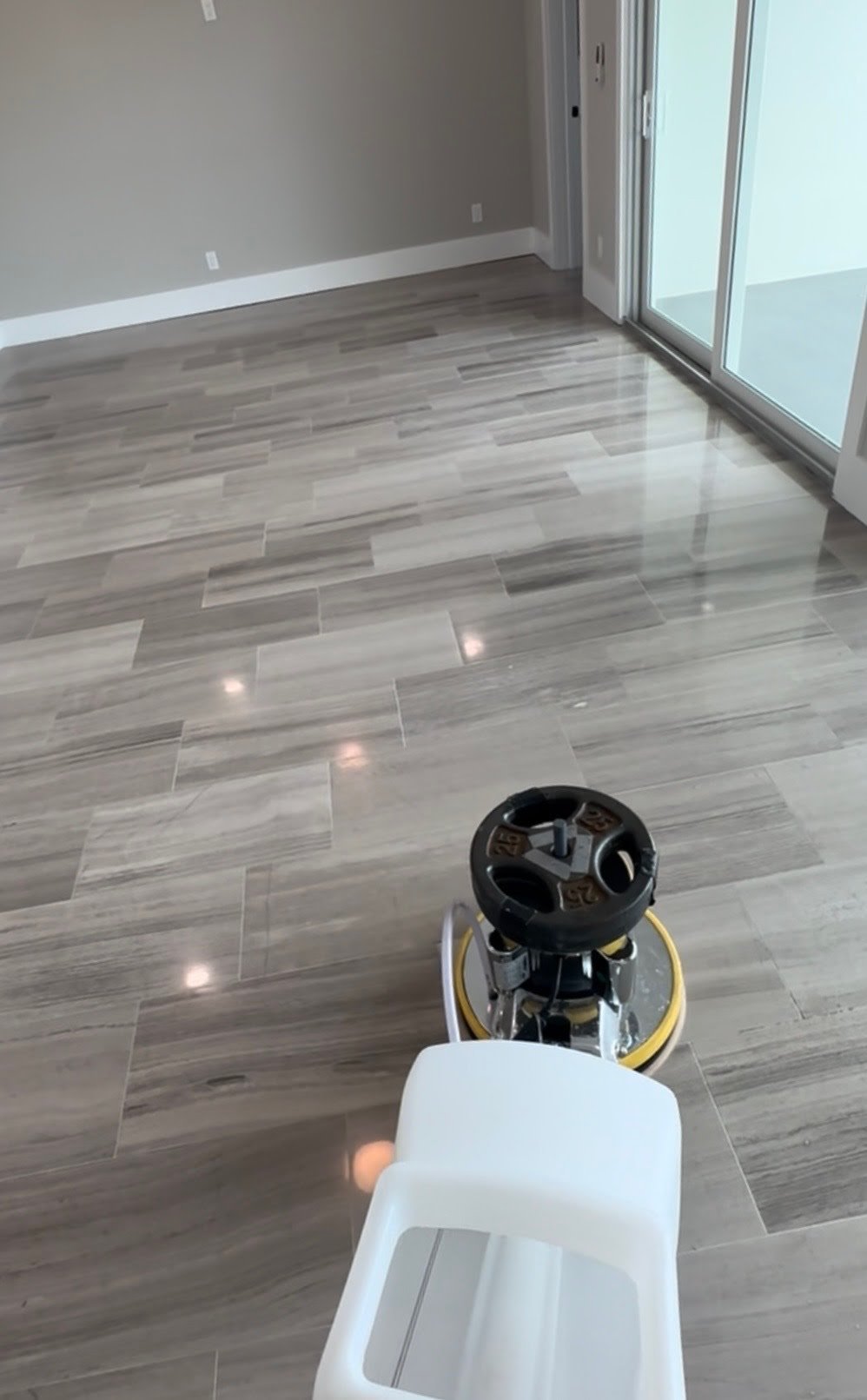Empty room with gray wood-look tile flooring, a sliding glass door, and a small machine cleaning the floor.