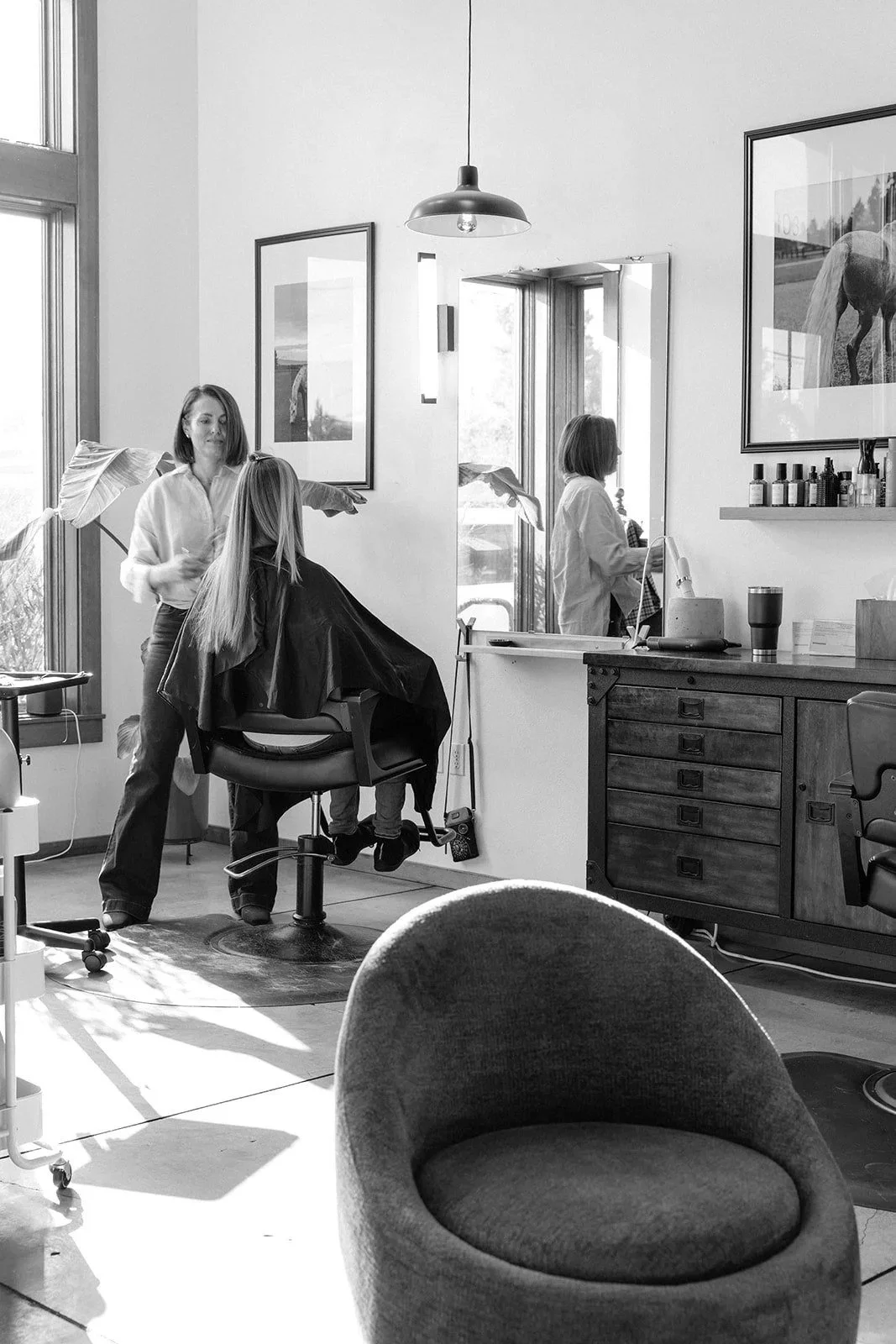 Hair stylist styling a client's hair in the bright, plant-filled styling room at Slate in Bend, Oregon