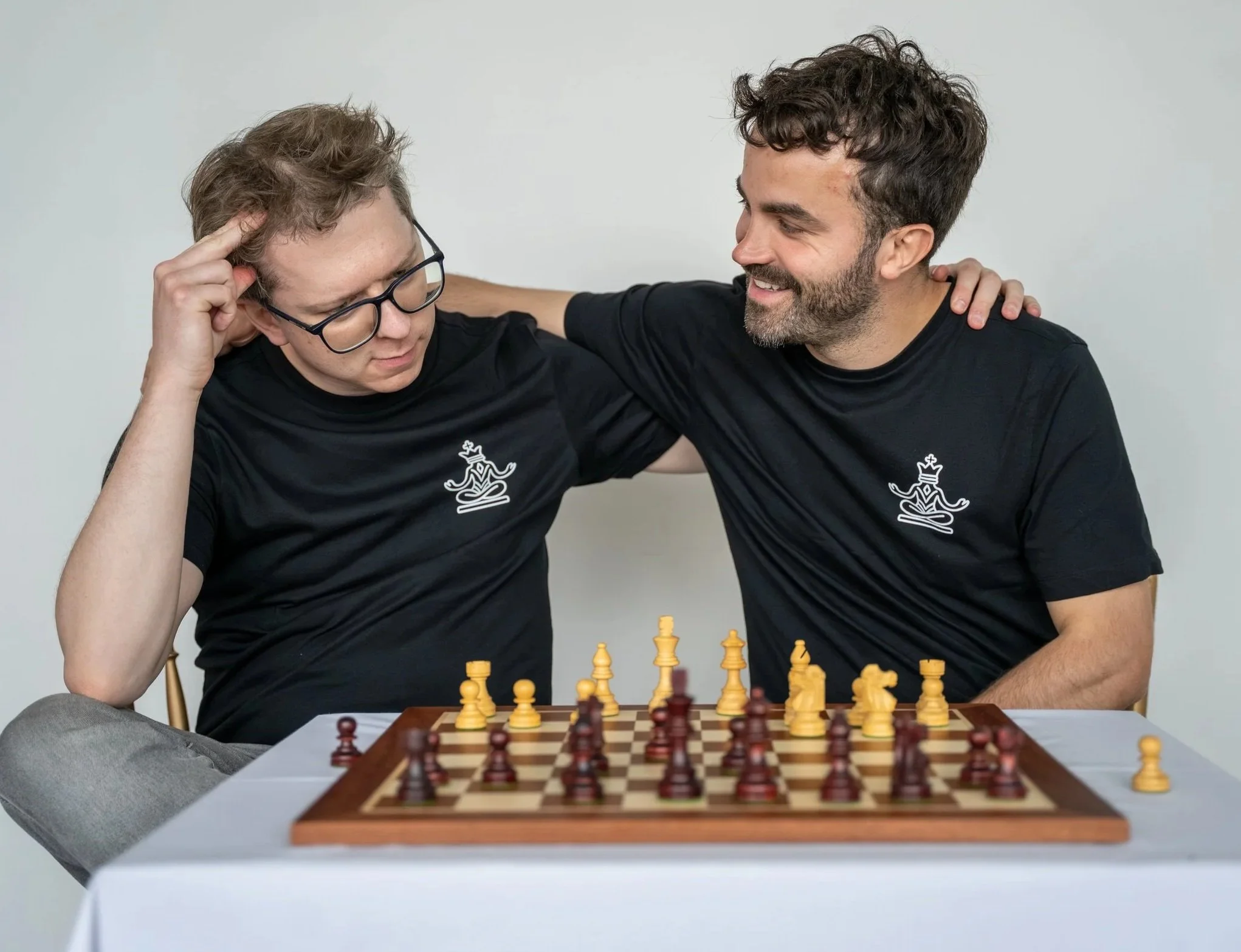 Two men playing chess at a table, smiling, with a chessboard in the foreground.