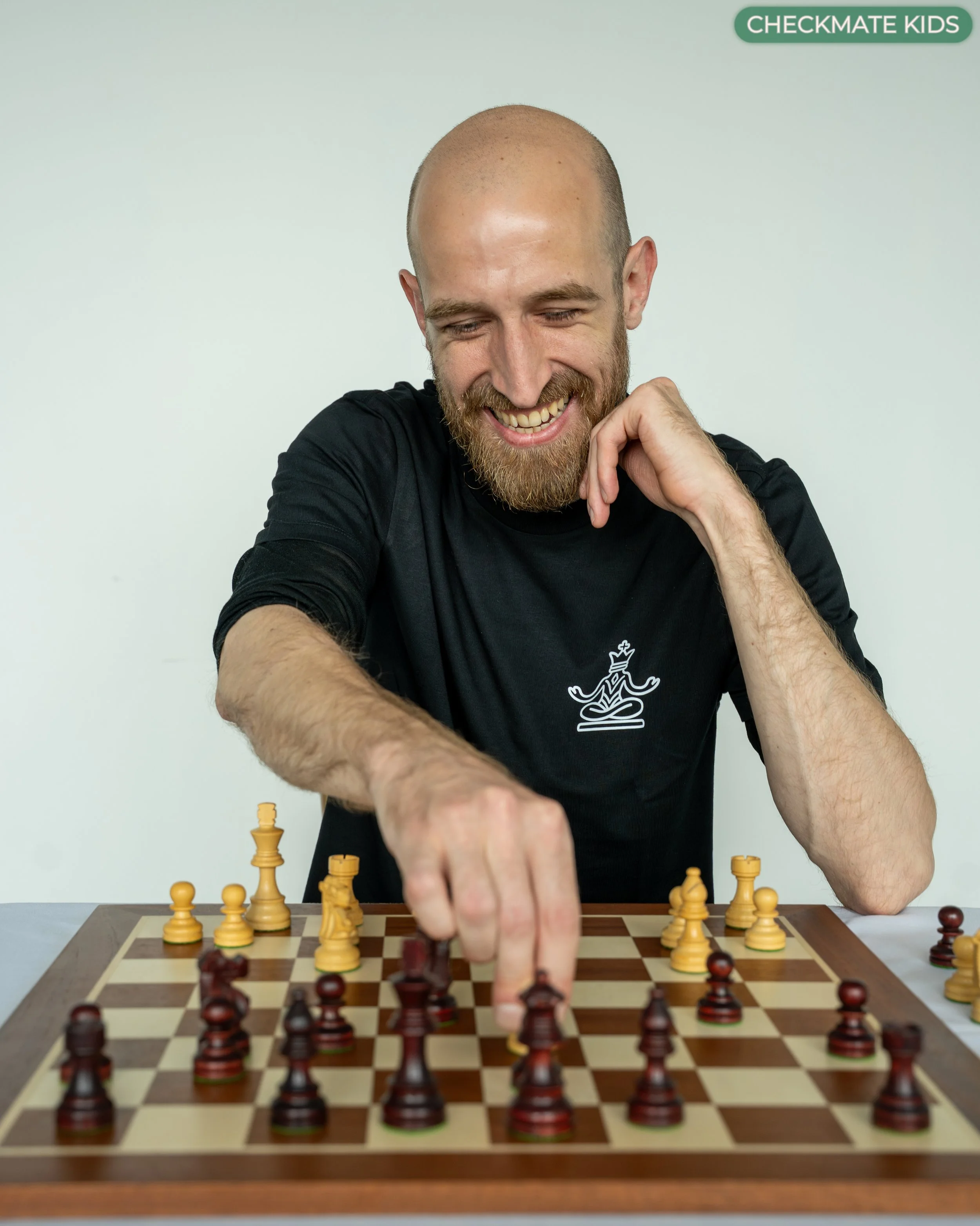A man with a beard and bald head playing chess, making a move on the chessboard.