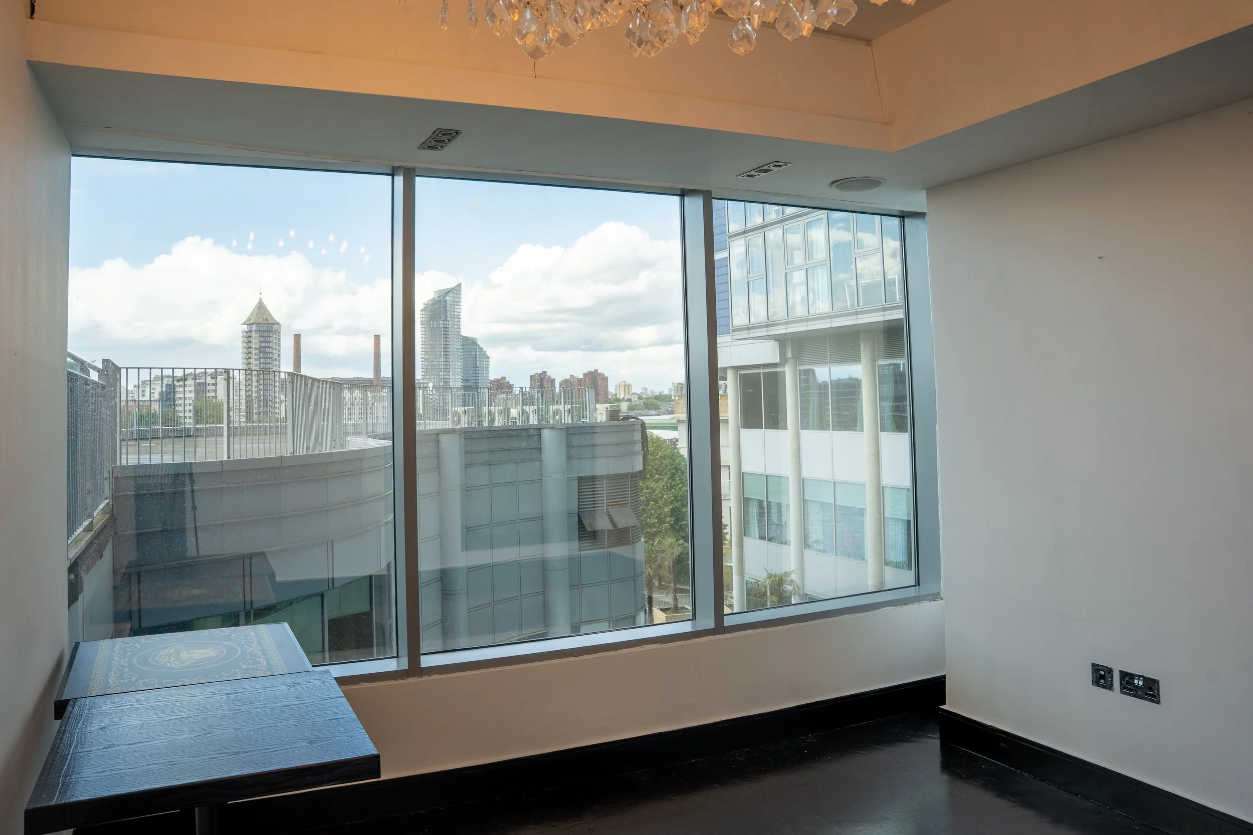 View of a city skyline through large glass windows in a modern room, with some buildings visible in the background and a small section of an outdoor terrace.