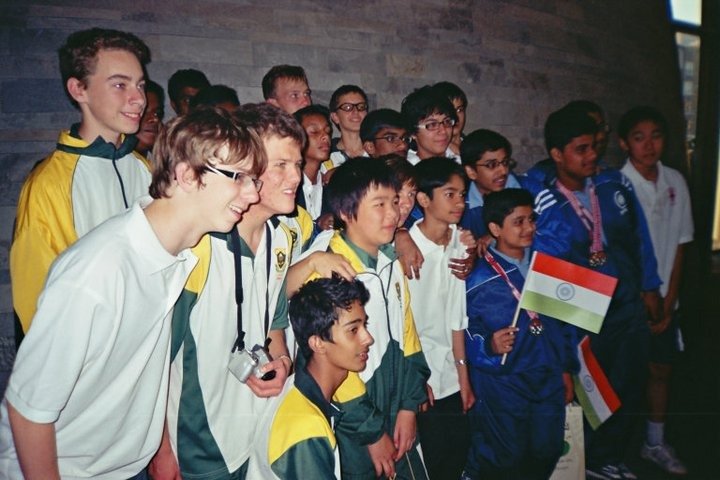Group of children and teenagers posing for a photo, some holding Indian flags, in a school or community center setting.