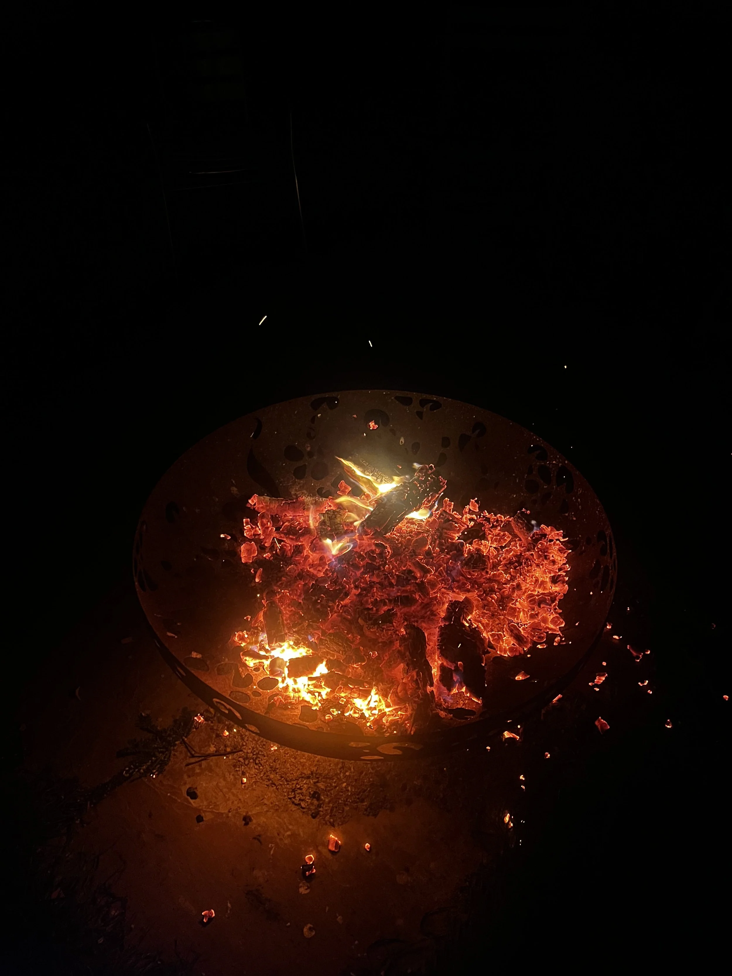 A small fire in a metal container with glowing embers and wood burning in the darkness.