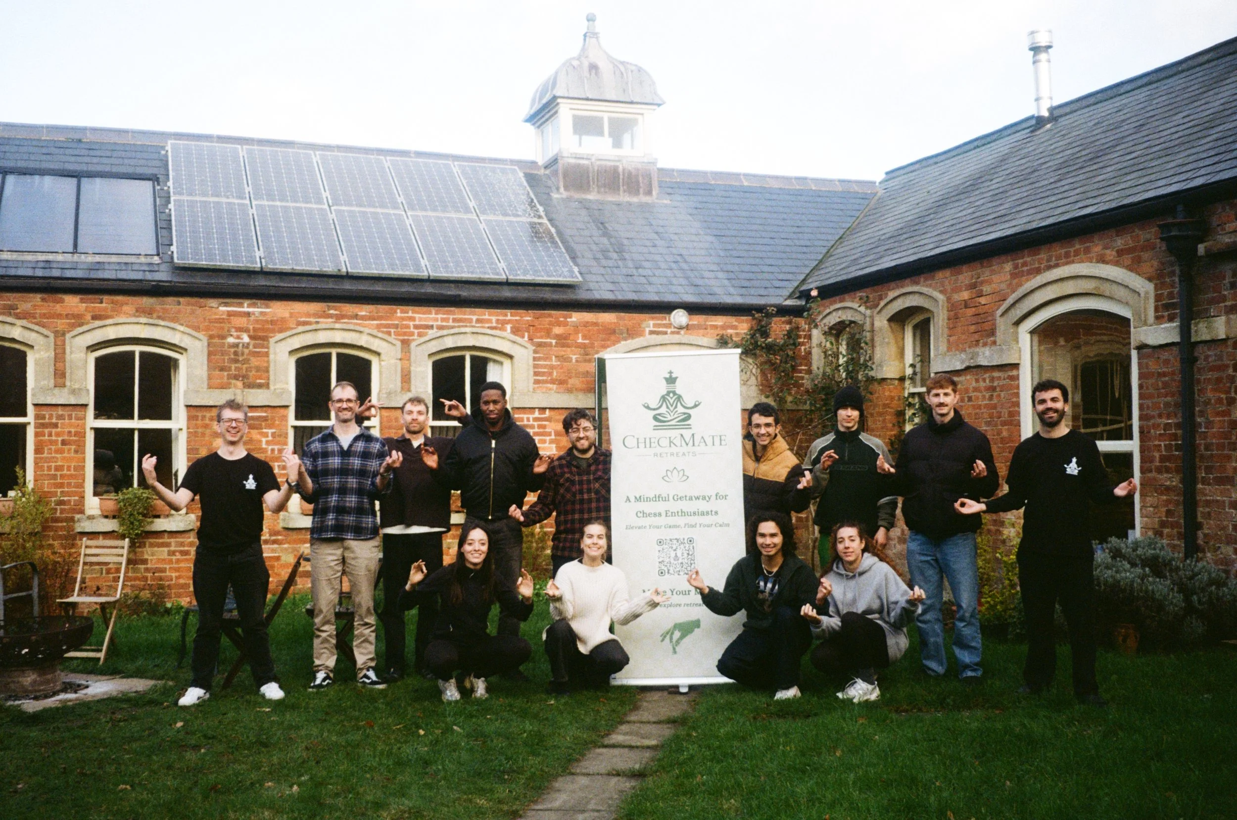 Group of young adults posing with a Checkmate Retreats banner in front of a brick house with solar panels on the roof.
