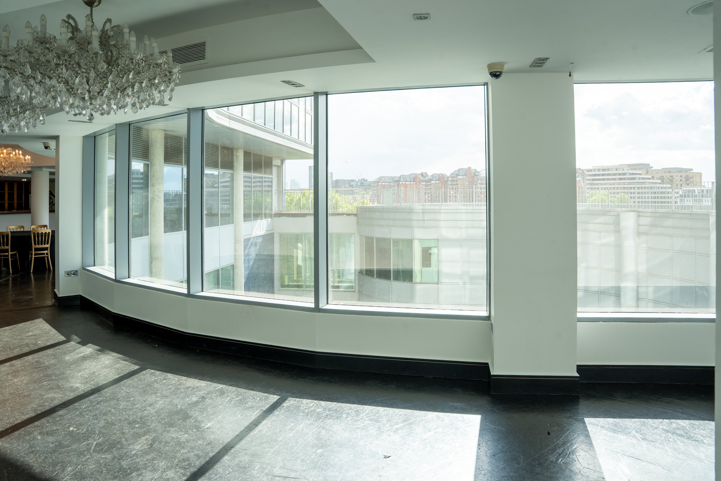Modern interior with large floor-to-ceiling windows, a chandelier, and a view of city buildings outside.