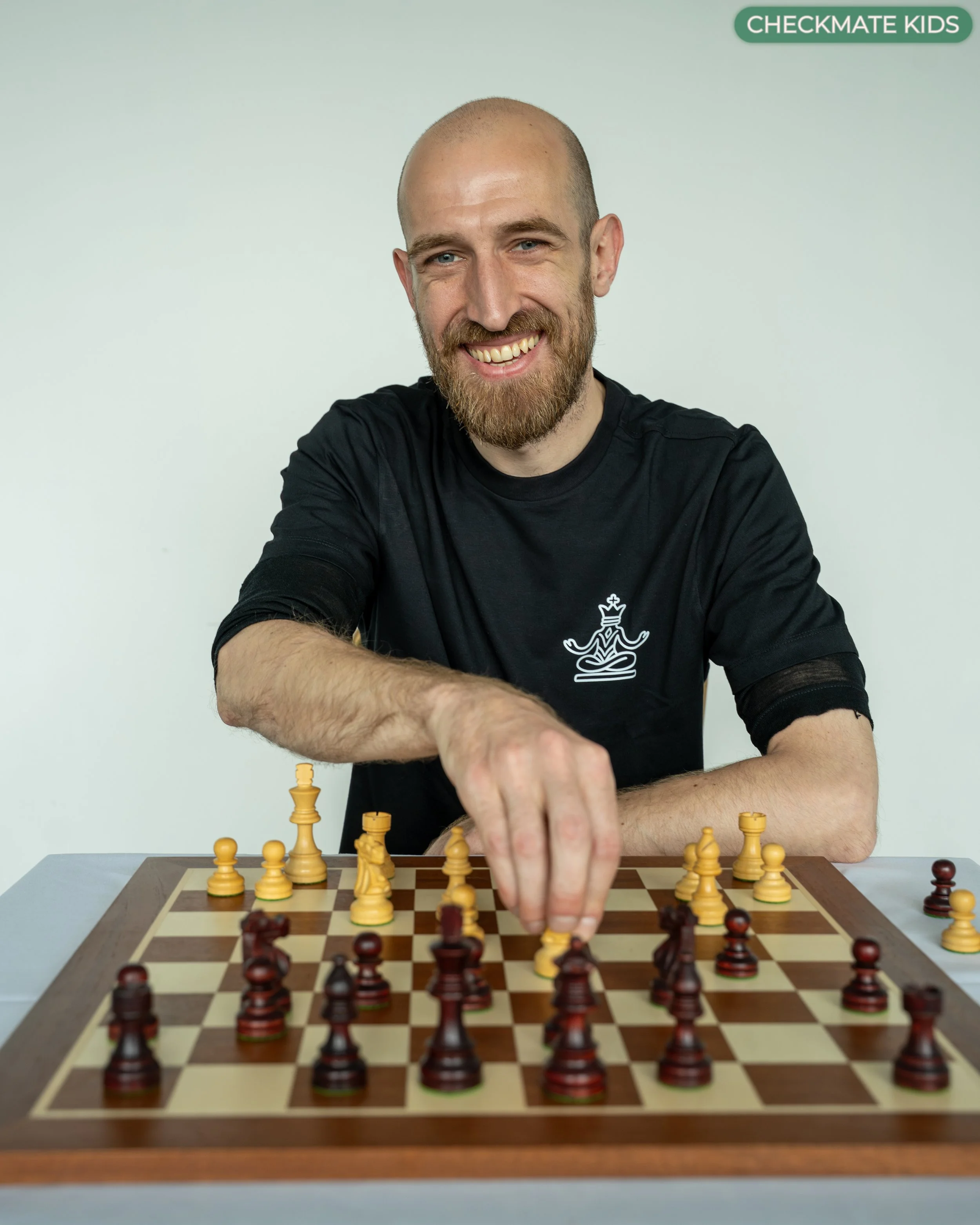 Man with a beard playing chess, reaching to move a piece on the game board.
