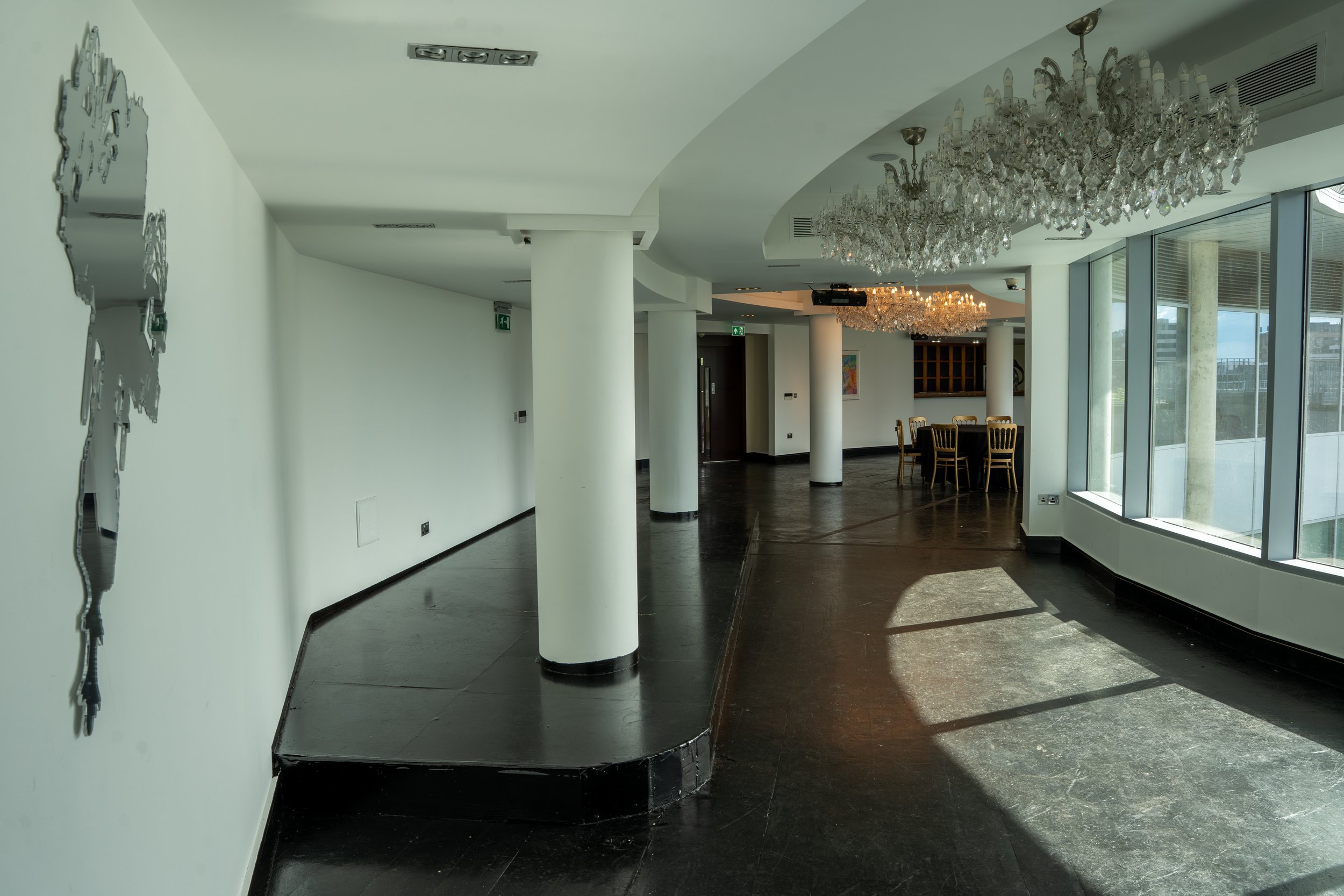 Modern interior space with white walls, large windows, a shiny crystal chandelier, round wooden dining table with chairs, and decorative artwork.