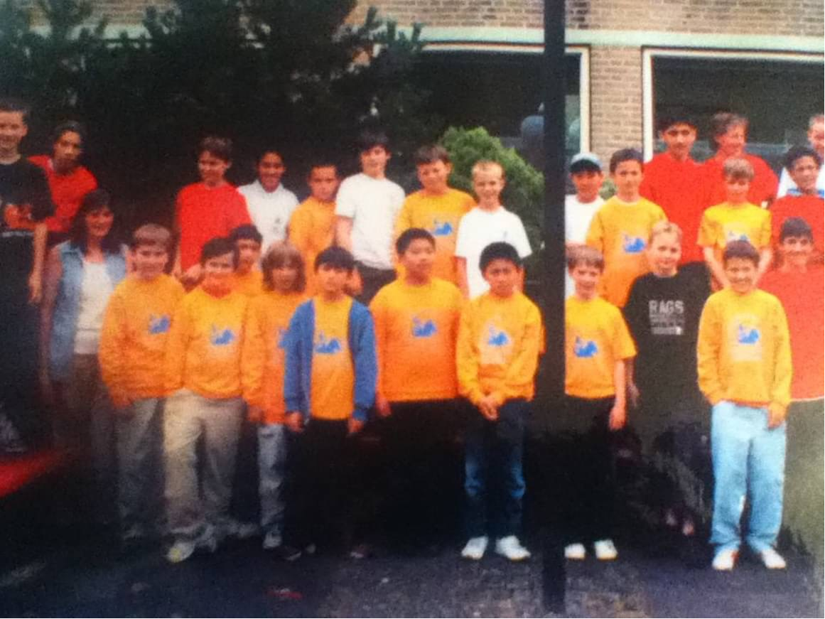 Group of children and teenagers posing outdoors in front of a building, with some wearing yellow sports jerseys.