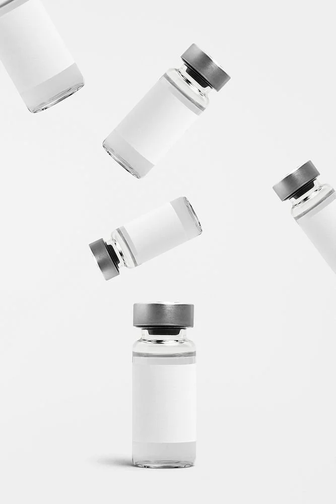 Multiple small glass vials with gray caps and blank labels, some floating in mid-air and one standing upright, against a plain white background.