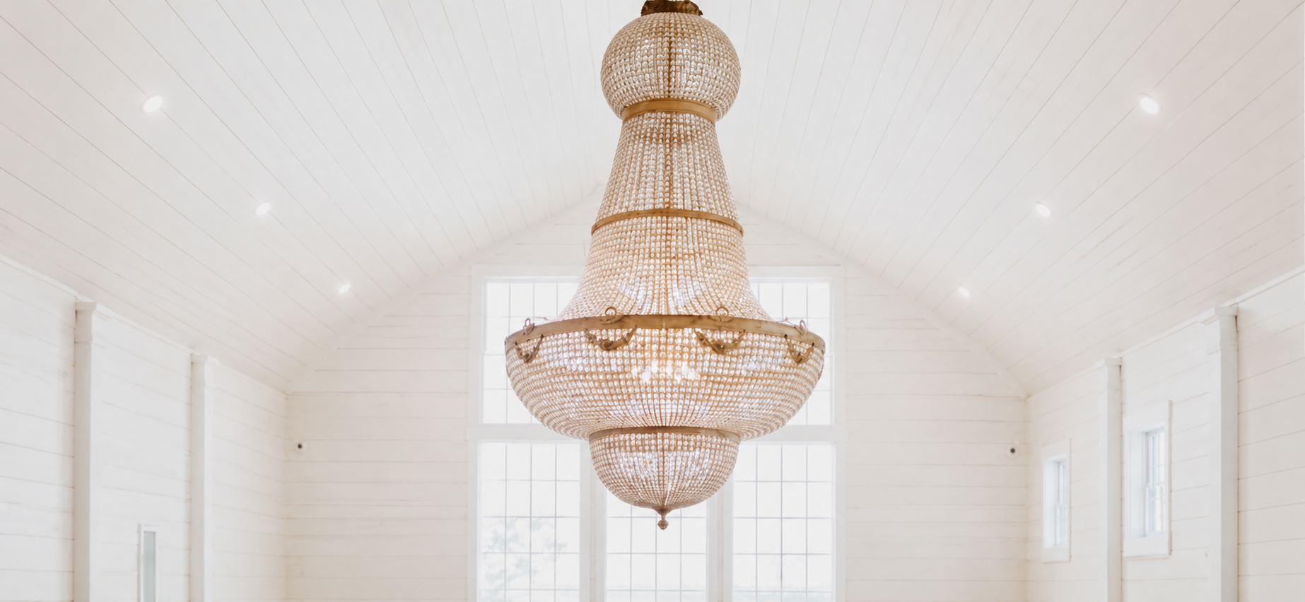 Large ornate chandelier hanging from a white ceiling inside a bright room with large windows.