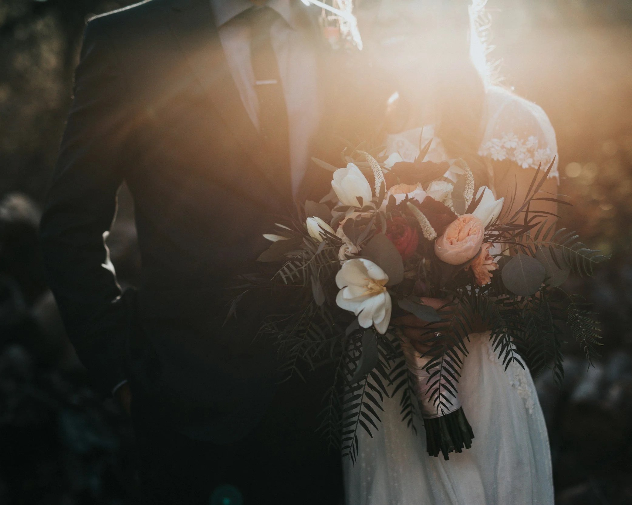 A person holding a bouquet of flowers, standing outdoors, with sunlight creating a bright glow around them.