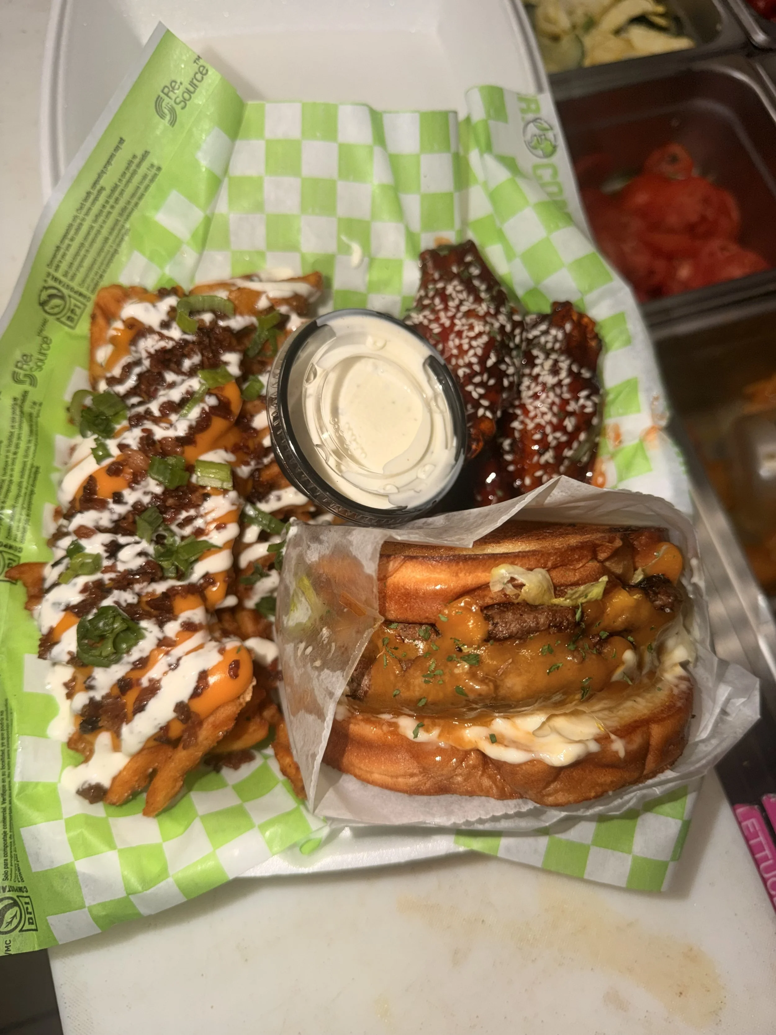 A tray of Mexican food with loaded tacos, shredded meat sandwiches, and a container of sliced tomatoes in the background.