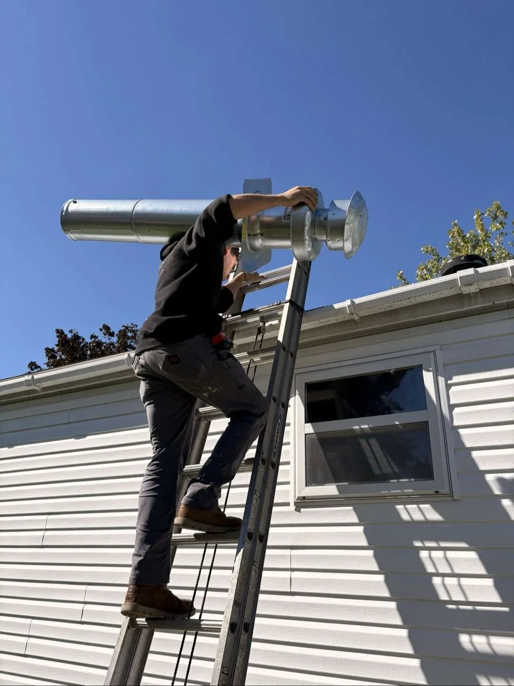 Installation technician climbing a ladder to replace the furnace roof jack on a mobile home