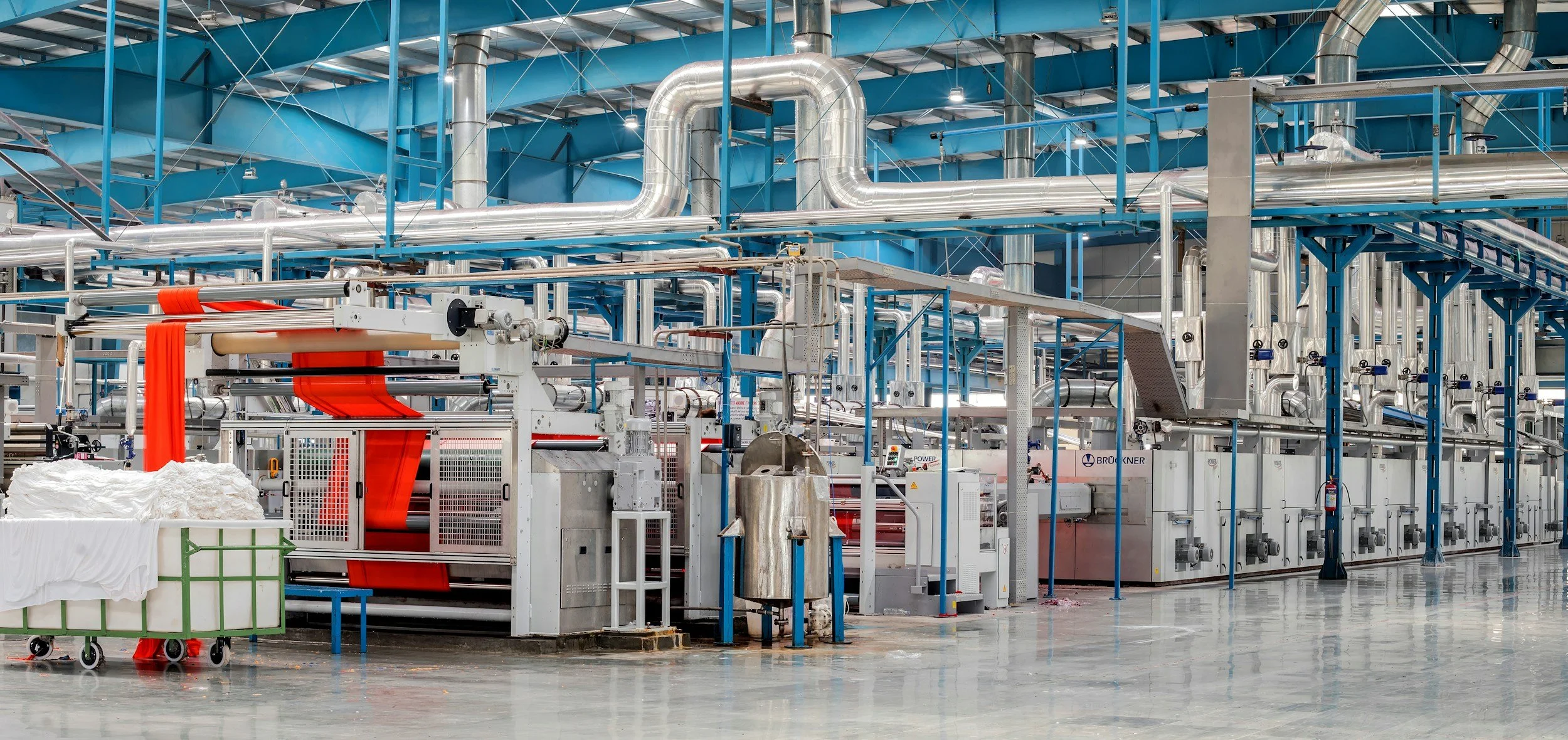 Industrial manufacturing factory with large machinery, pipes, and conveyor belts in a spacious clean plant.