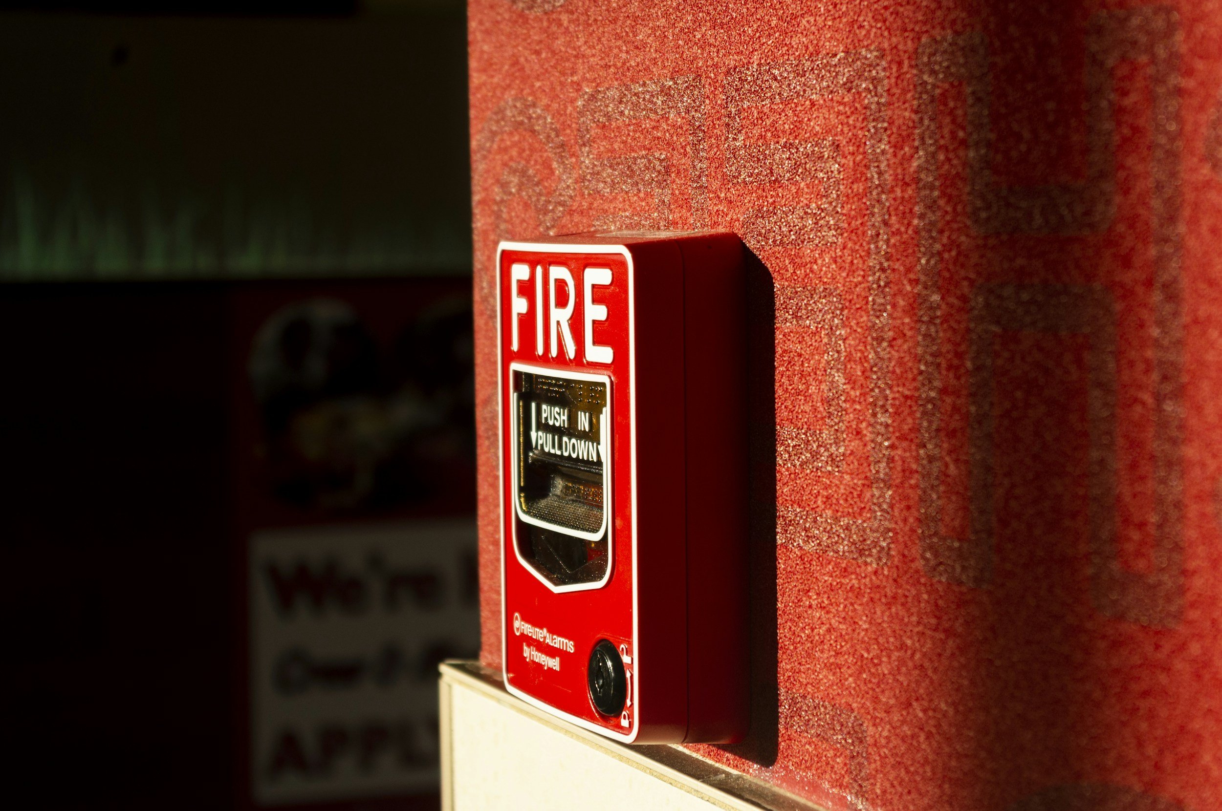 Red fire alarm pull station mounted on a red textured wall.