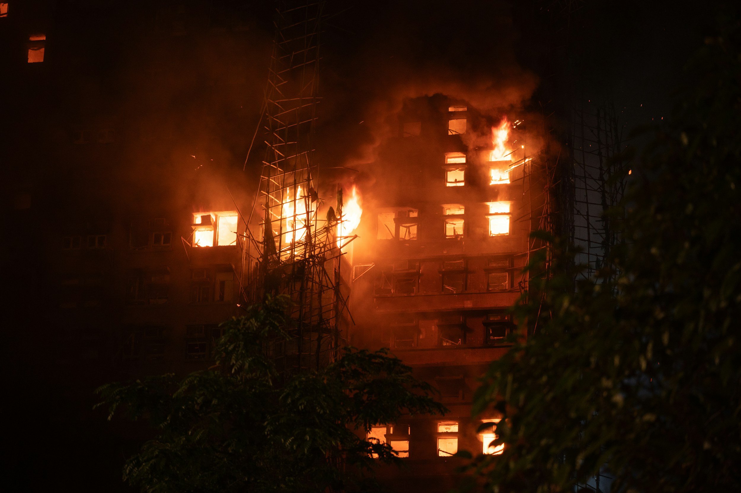 Nighttime photo of a building on fire with flames and smoke, surrounded by metal structures.