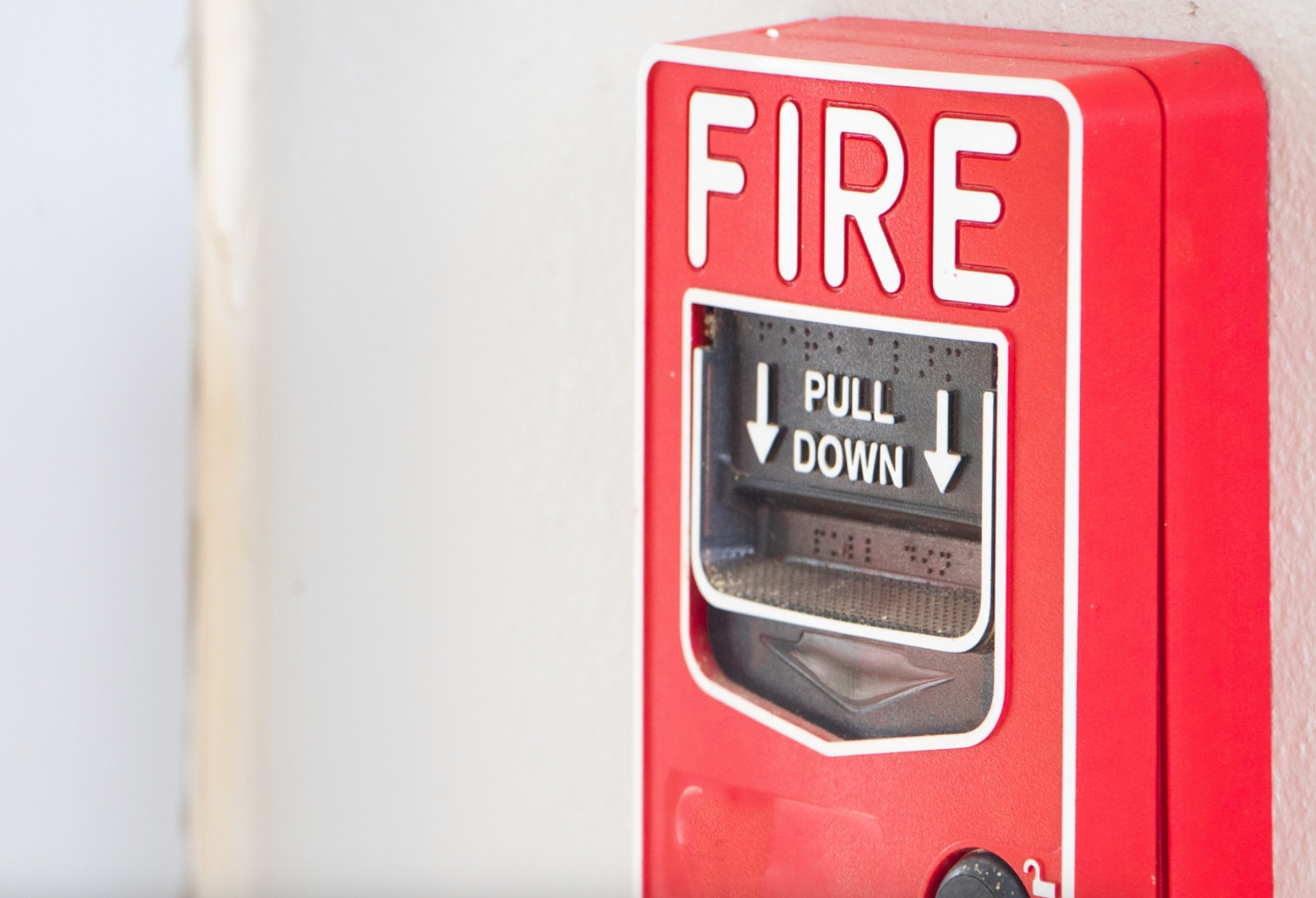 A red fire alarm on a light-colored wall with white text reading 'FIRE' and black directional buttons labeled 'PULL' and 'DOWN.'