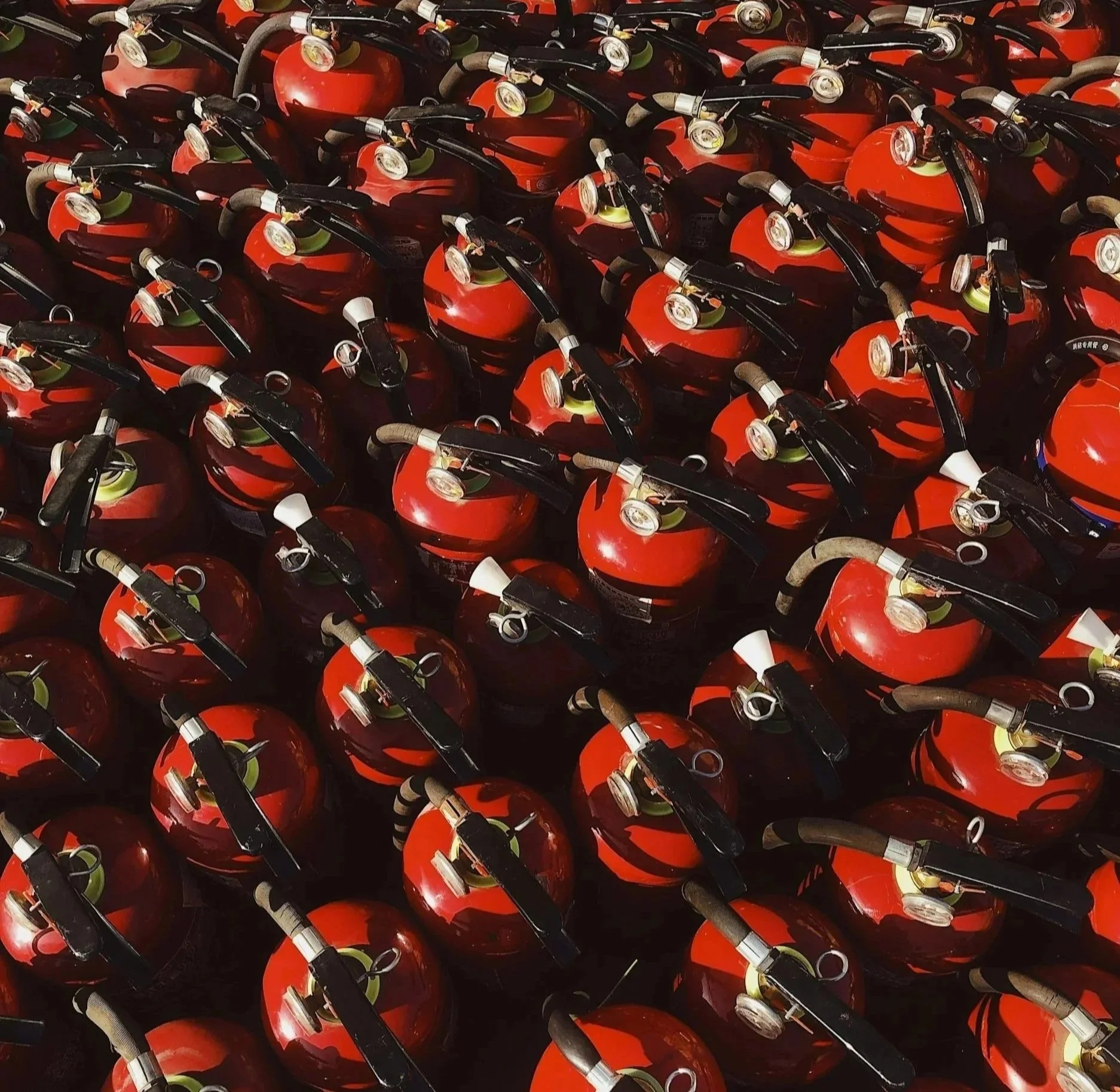 A large number of stacked red fire extinguishers with black handles and white pressure gauges.