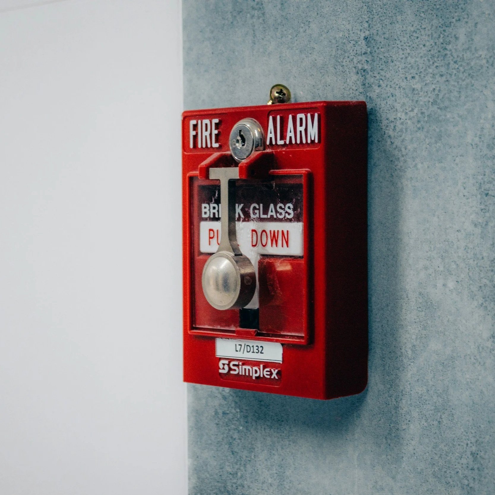 Red fire alarm with labeled switch and instructions, mounted on a wall.