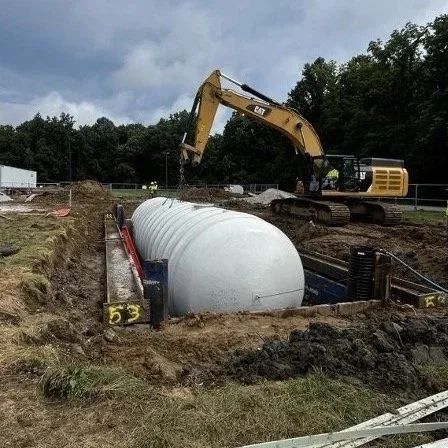 Construction site with an excavator and a large white cylindrical tank being installed underground.