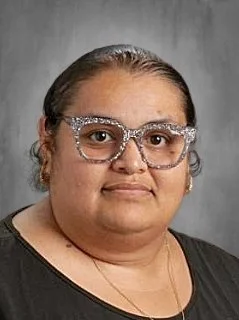 A woman with glasses wearing a black top against a gray background.