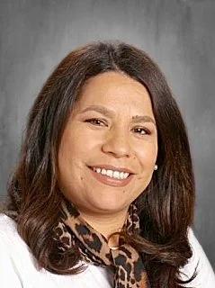 Portrait of a woman with shoulder-length brown hair, smiling, wearing a white top and a patterned scarf.