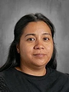 Portrait of a woman with medium skin tone, dark hair, and wearing a black shirt, posing against a gray background.