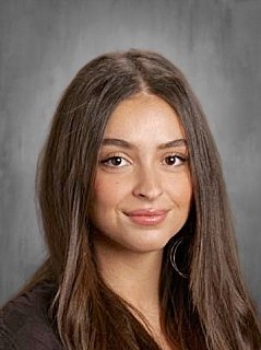 A young woman with long brown hair, smiling softly, against a gray background.