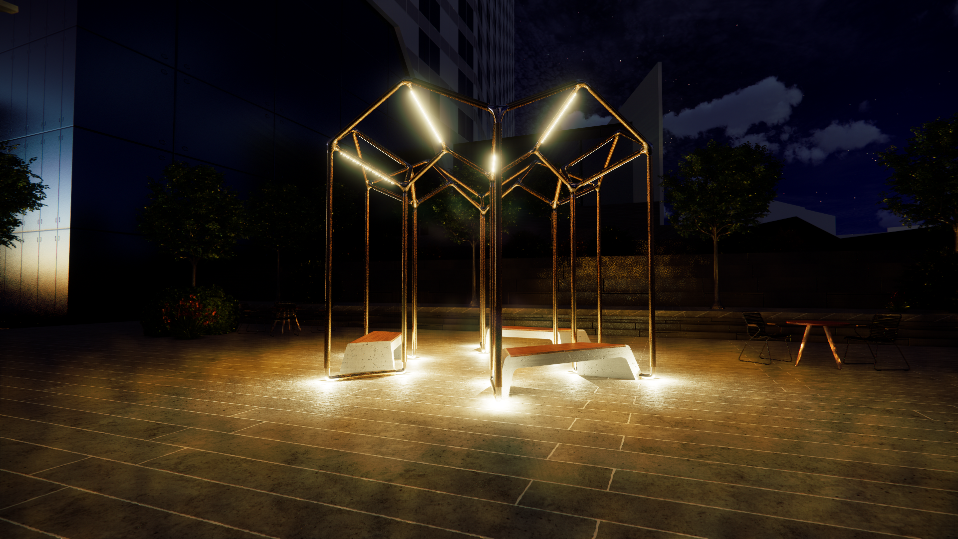 Nighttime view of an illuminated outdoor art installation with geometric metal frames, benches, trees, and a seating area, against a dark sky with stars and clouds.