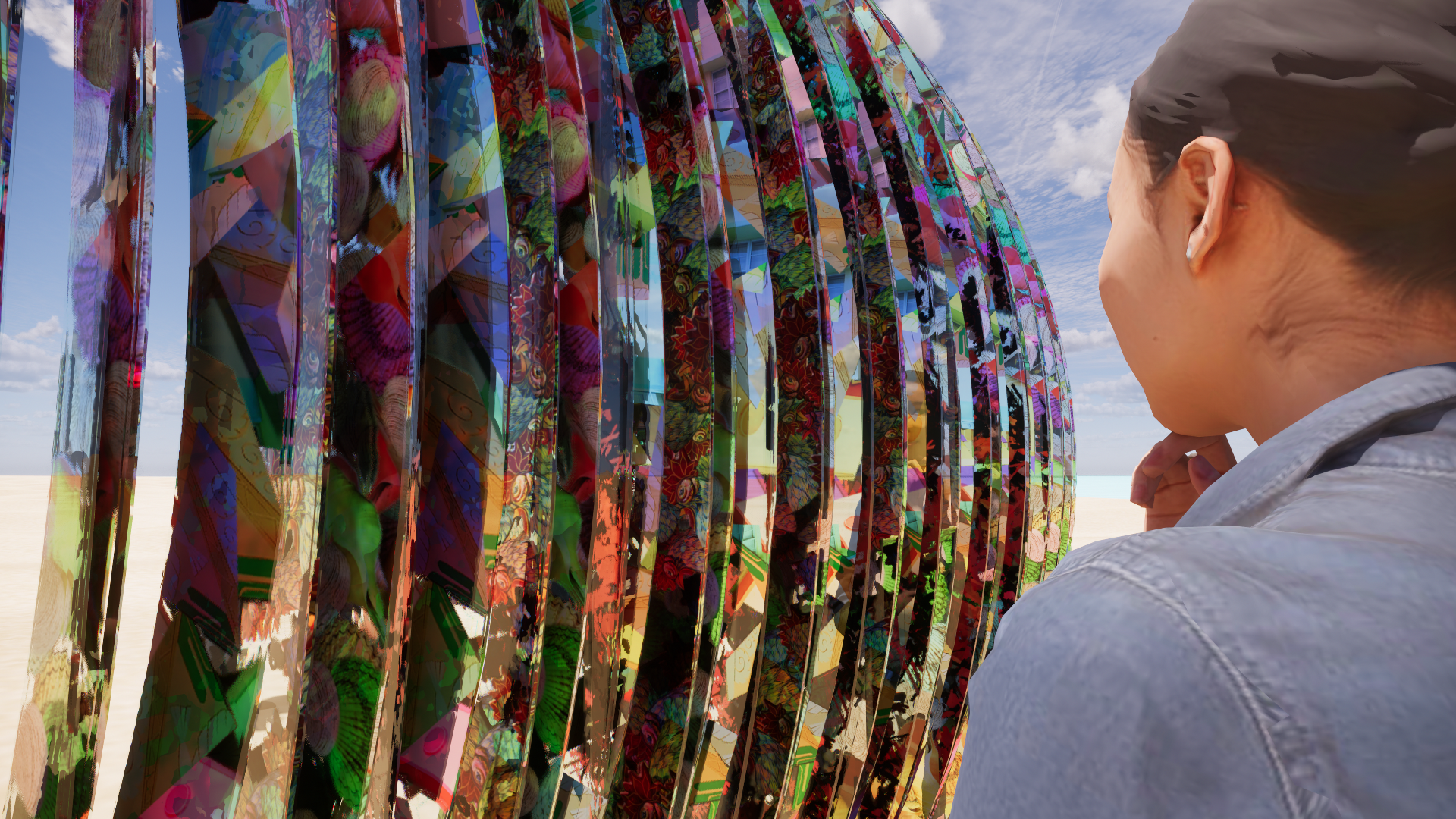 A woman with dark hair pulled back, wearing a gray jacket, stands outdoors on a sunny day, looking at a large, colorful, abstract sculpture made of vertical metallic panels with a mirror-like finish.