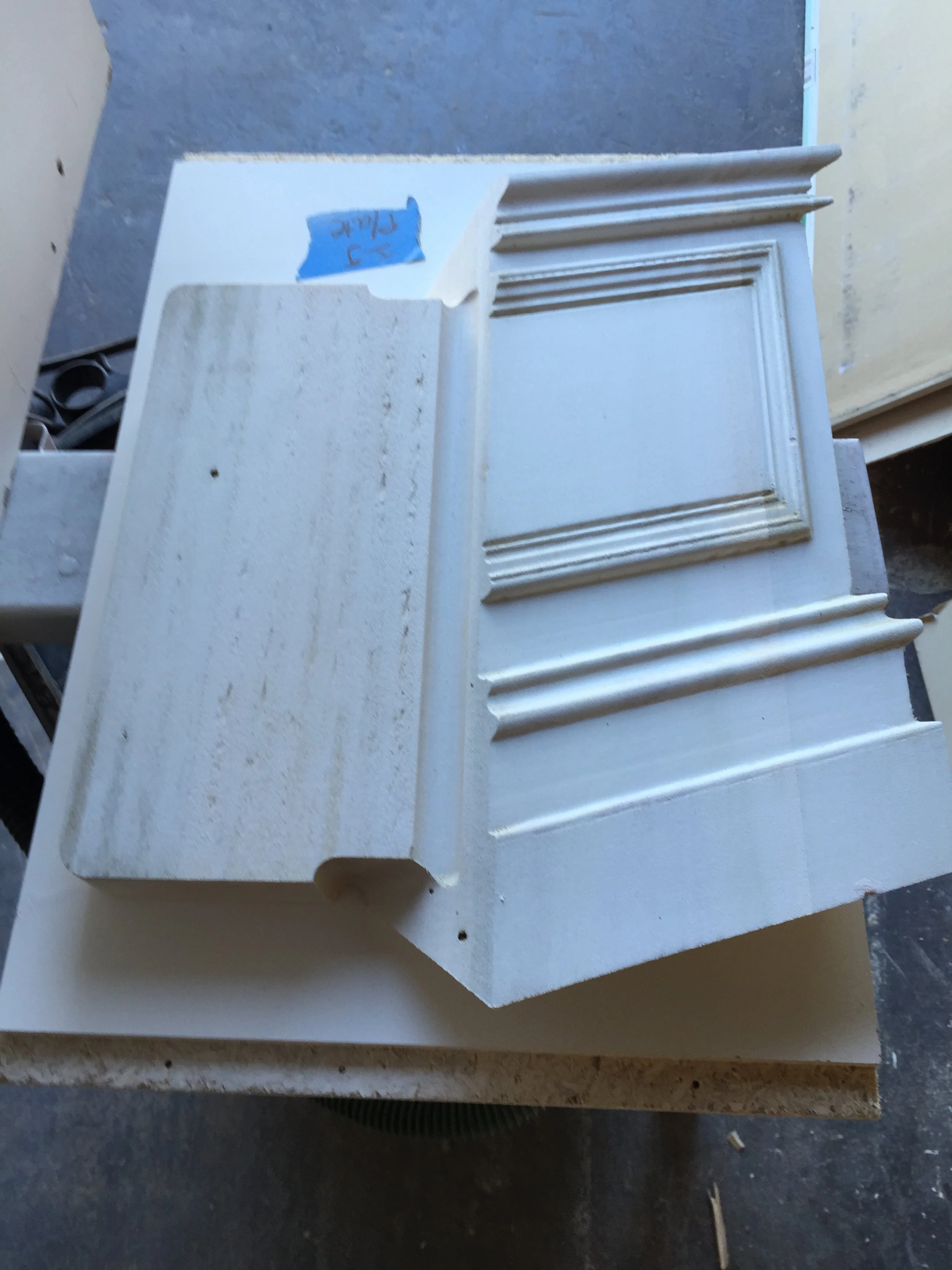 A white cabinet door with decorative molding, lying on a workbench in a workshop.