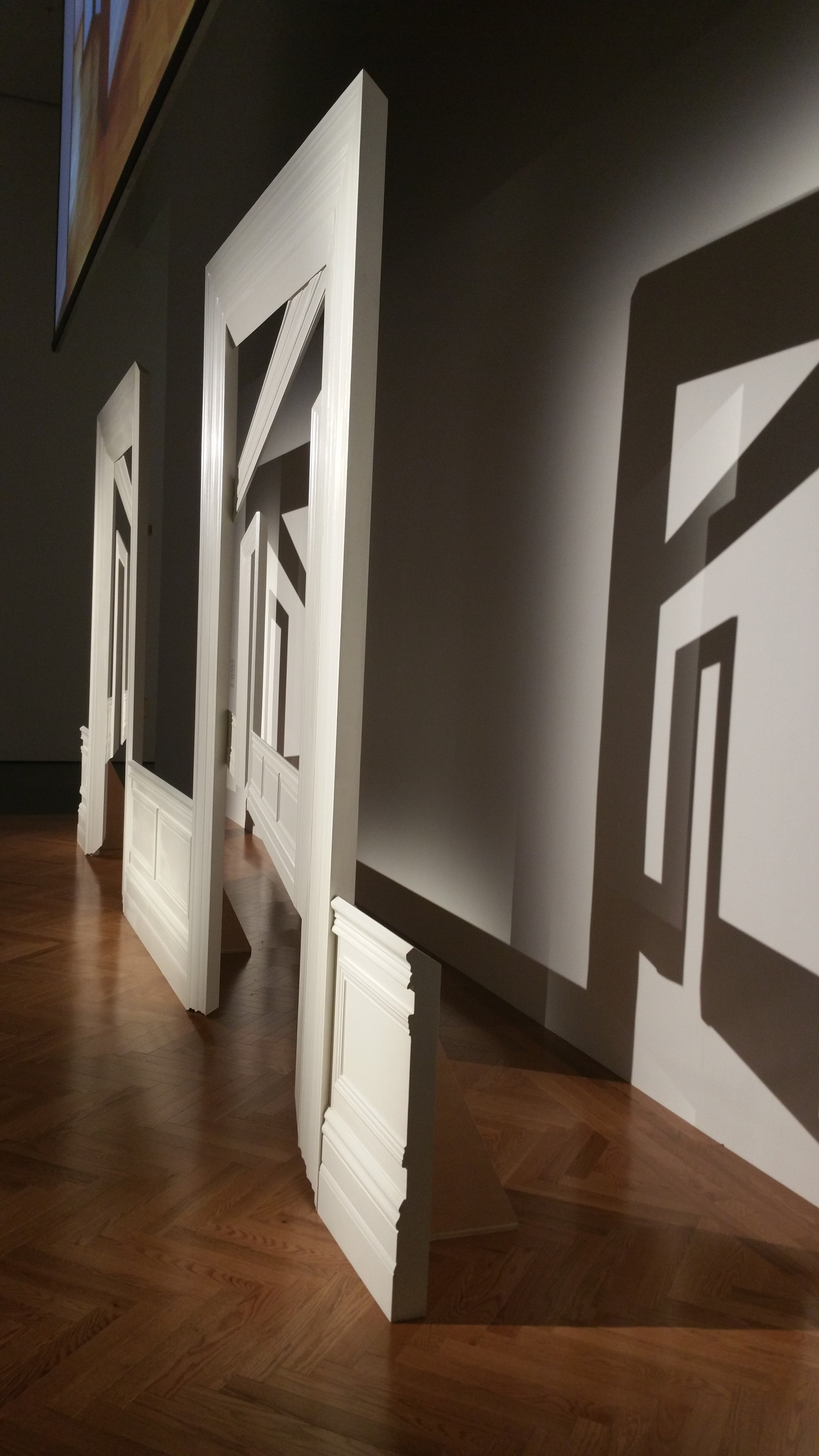 White wooden door frames and panels arranged on a wooden floor indoors, with shadows cast on a gray wall.