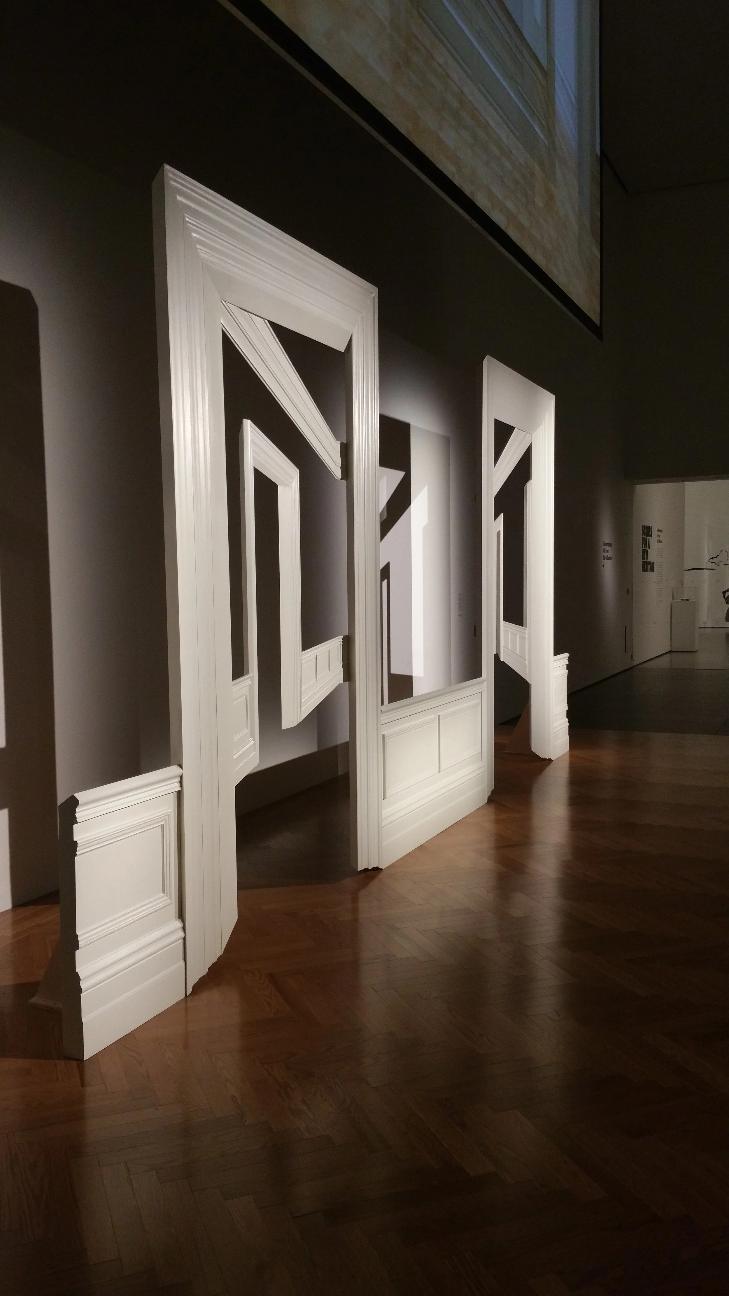 Empty room with white decorative wall panels and a wooden floor, with a large screen on the ceiling reflecting the room.
