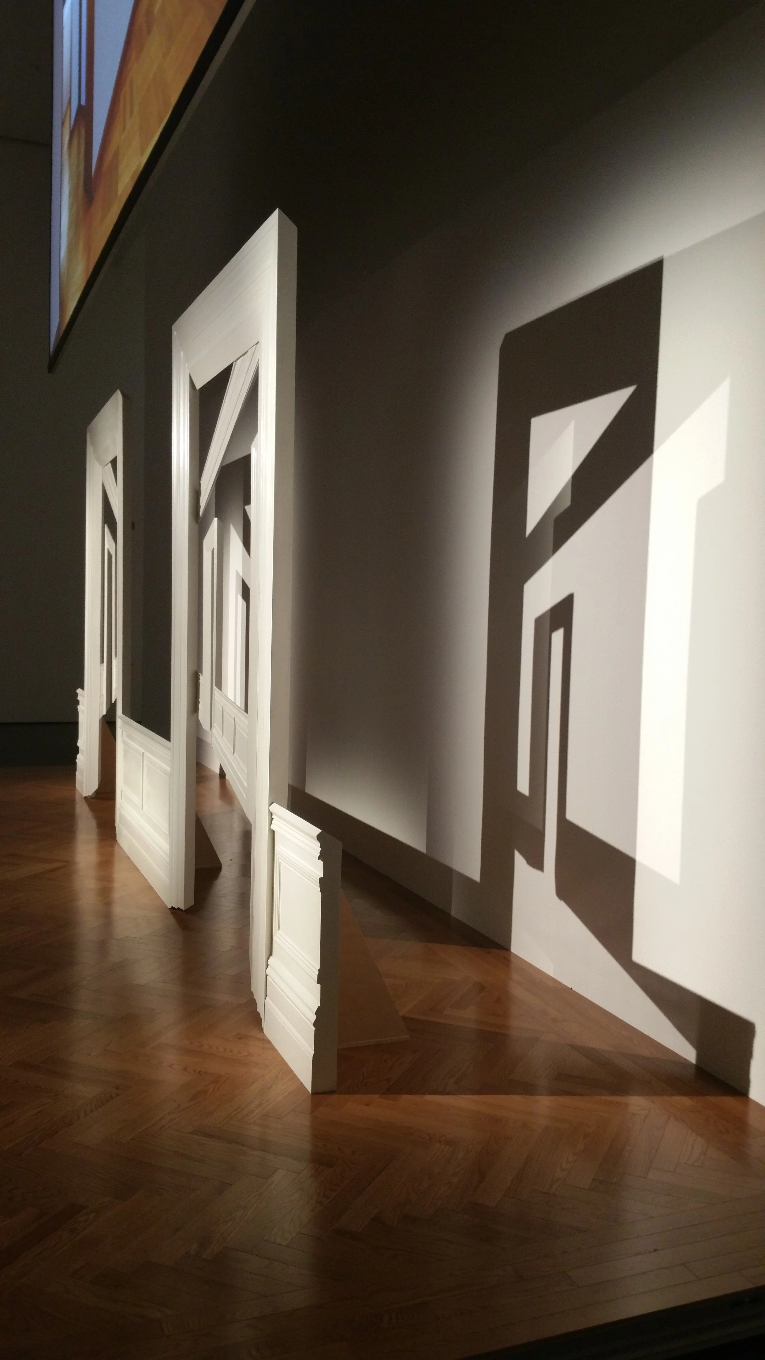 Display of multiple white picture frames casting shadows on a beige wall in a room with hardwood flooring.