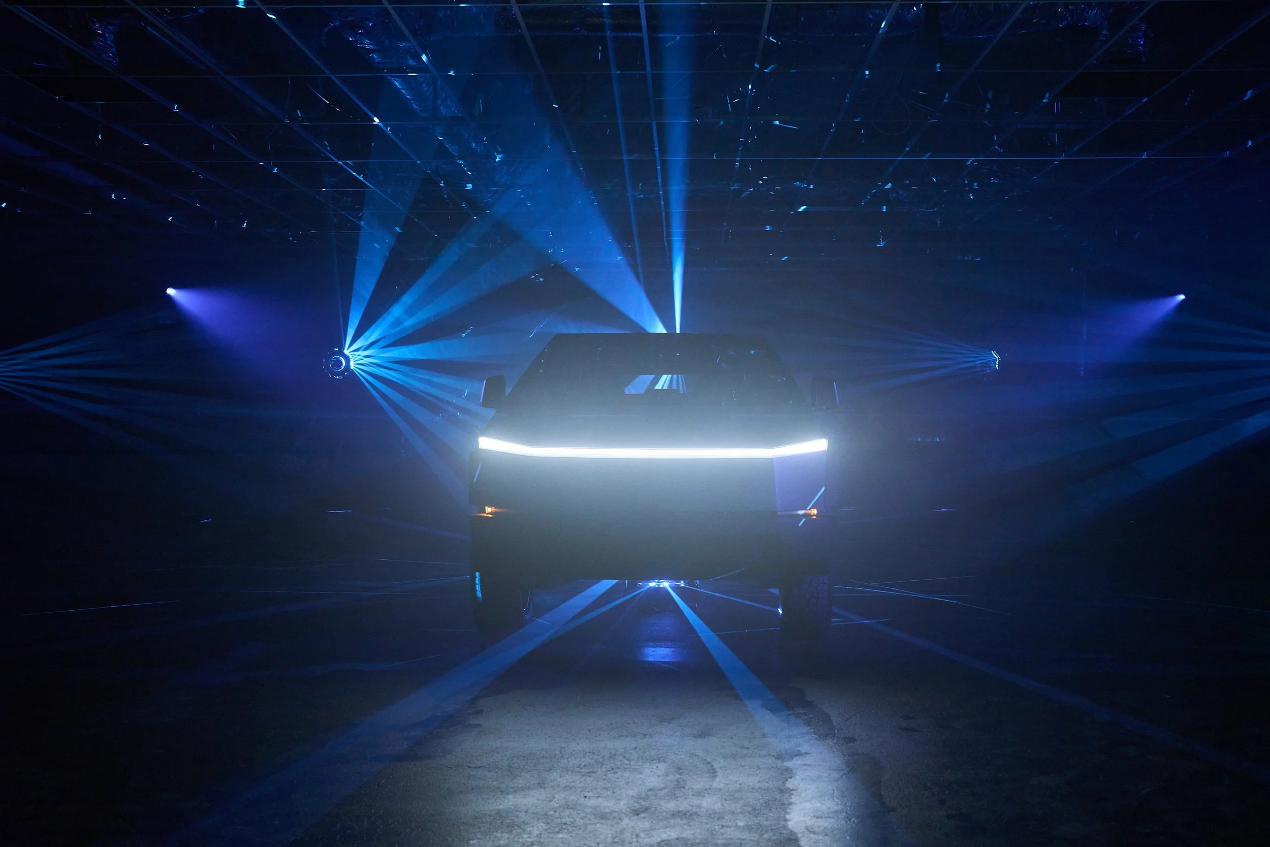 Dark indoor space featuring a black vehicle illuminated by blue laser lights and stage lighting.