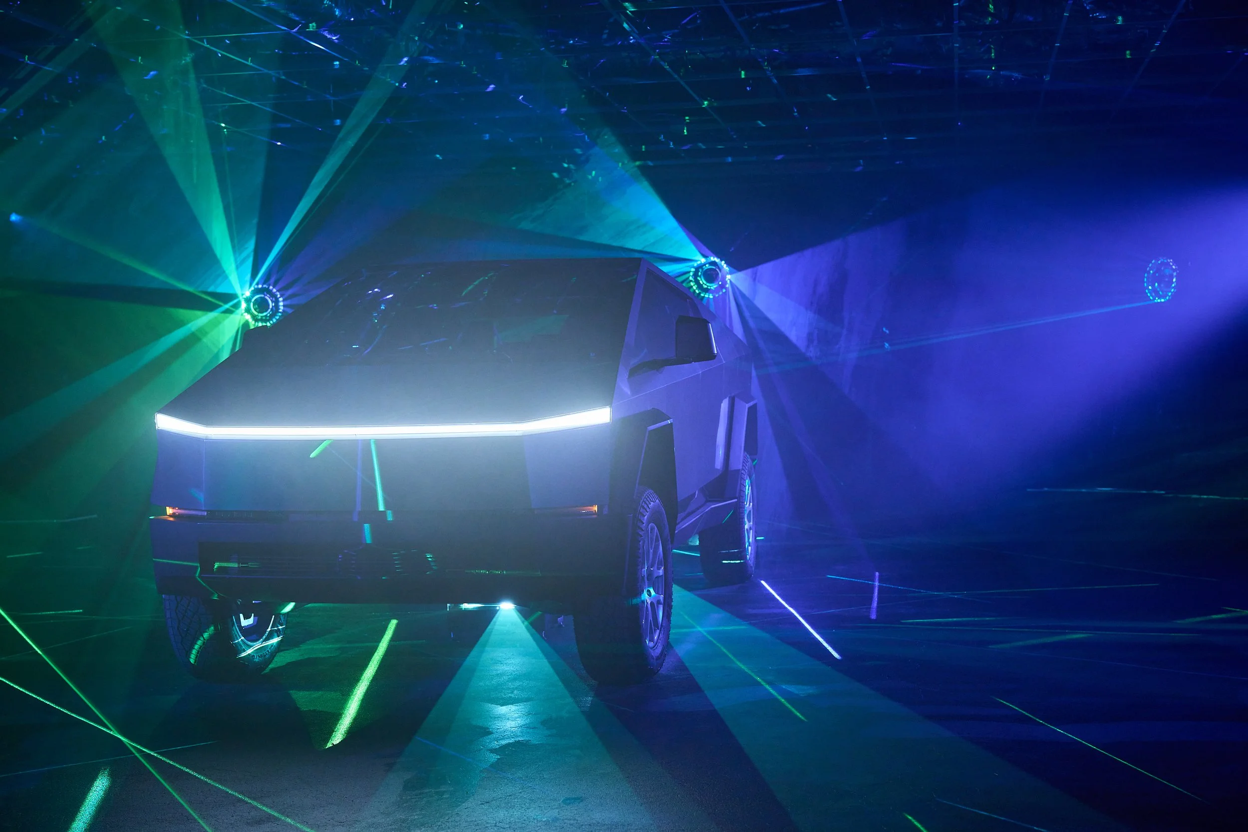 A car illuminated by green and blue laser lights in a dark room, creating a vibrant, futuristic atmosphere.