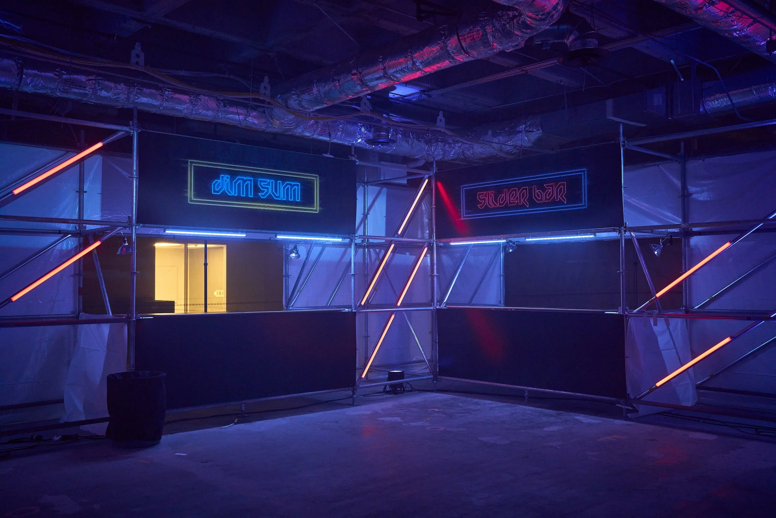 Interior of a nightclub or bar with neon signs reading 'djm sum' and 'studer bar', illuminated by colorful neon lights, with scaffolding and metallic ductwork visible on the ceiling.