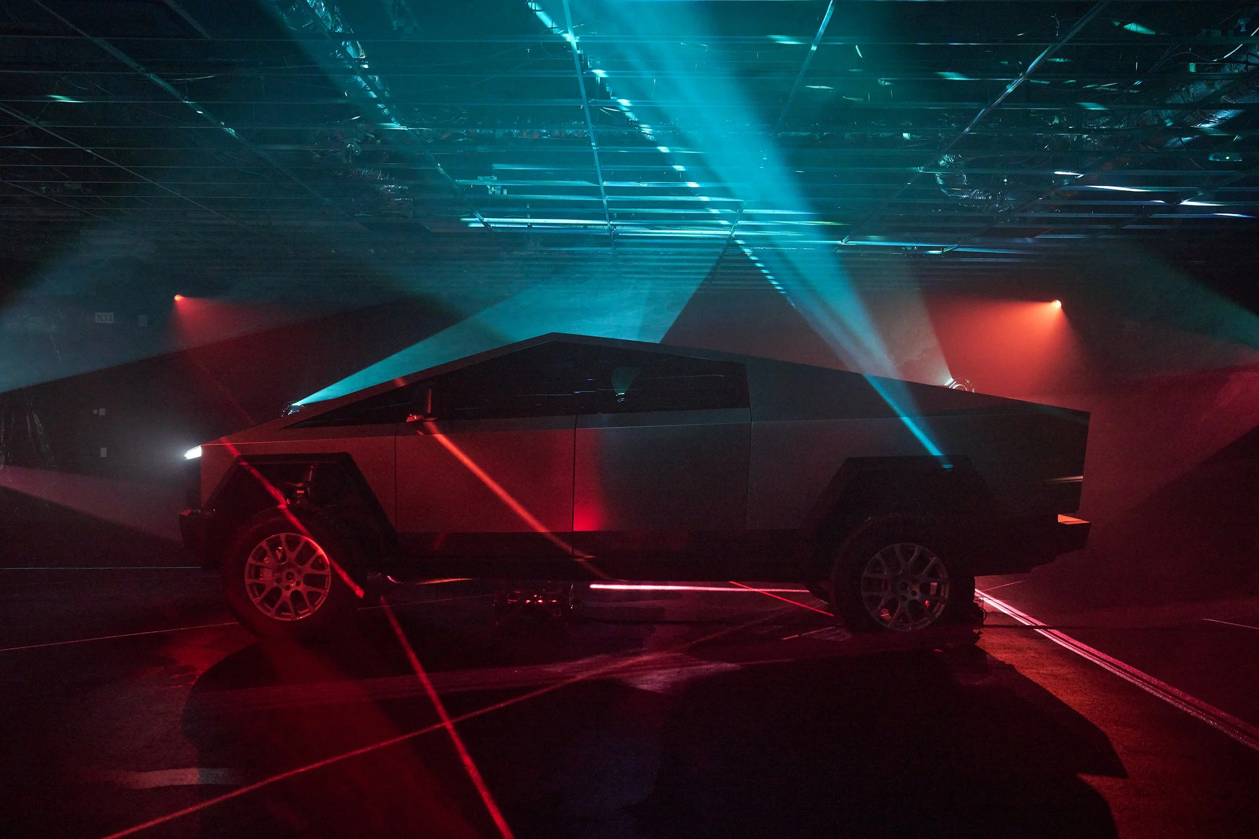 A black car illuminated by blue and red laser lights in a dark setting, with a reflective ceiling above.