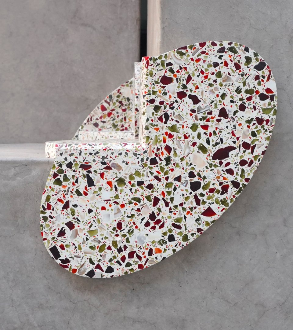 A modern, terrazzo-style decorative object with a colorful, speckled pattern of red, black, green, and white on a concrete surface.