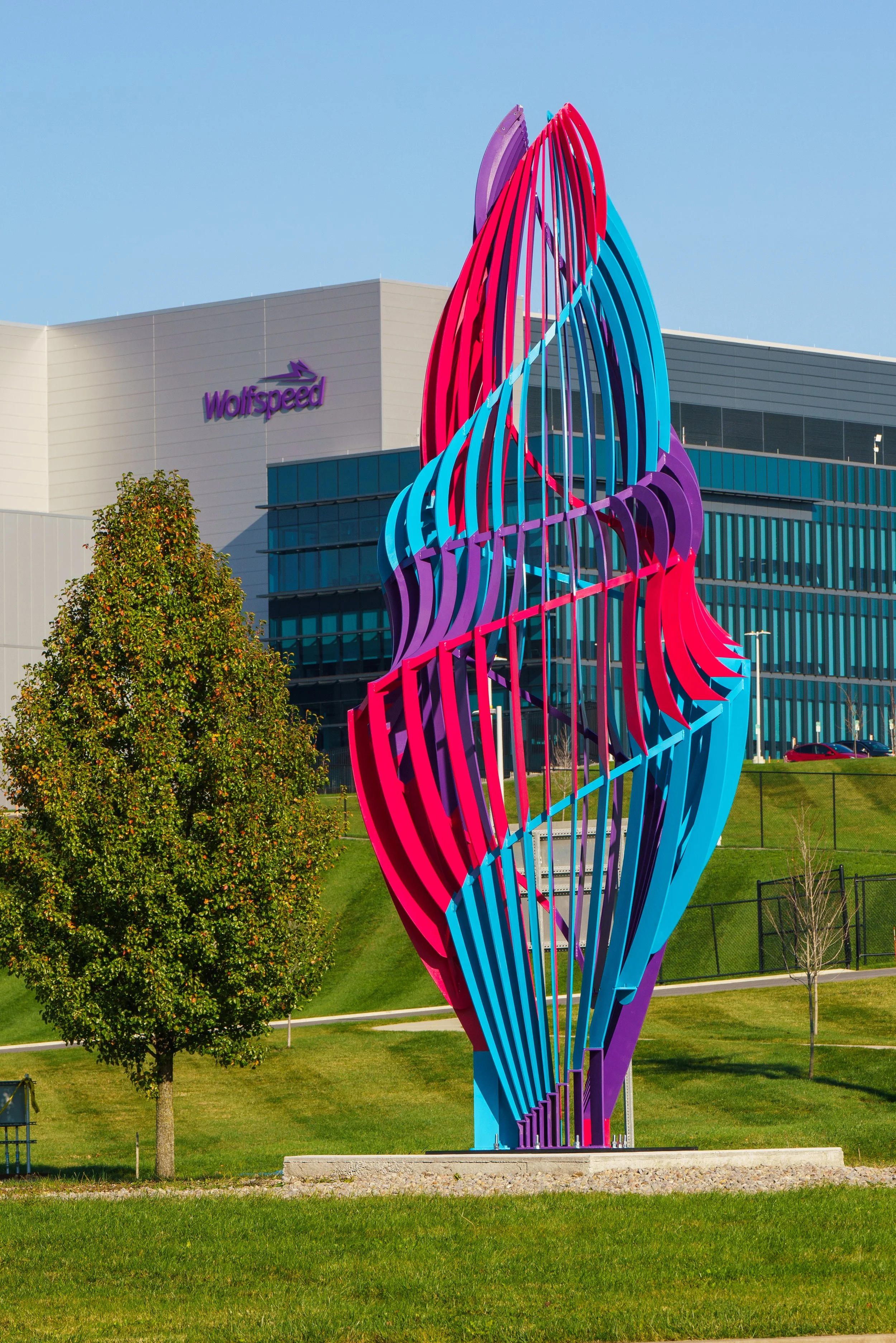 Colorful modern sculpture with arches in purple, blue, pink, and red in front of a corporate building with a Wolfspeed logo and a clear blue sky.
